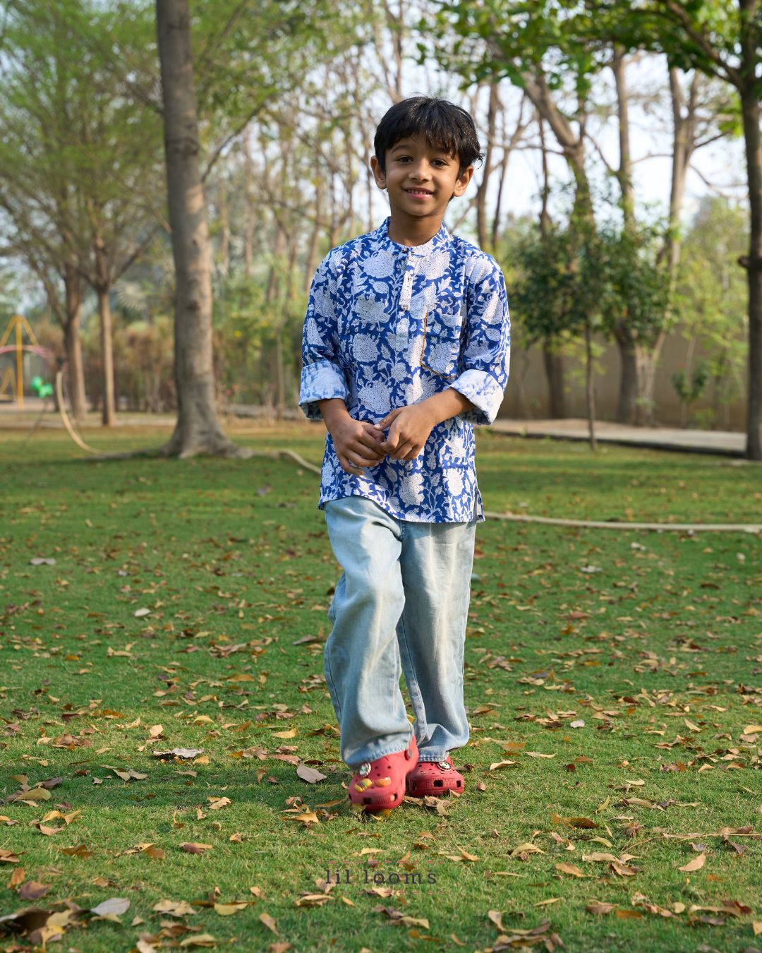 Child wearing a blue and white patterned shirt standing on grass with trees in the background