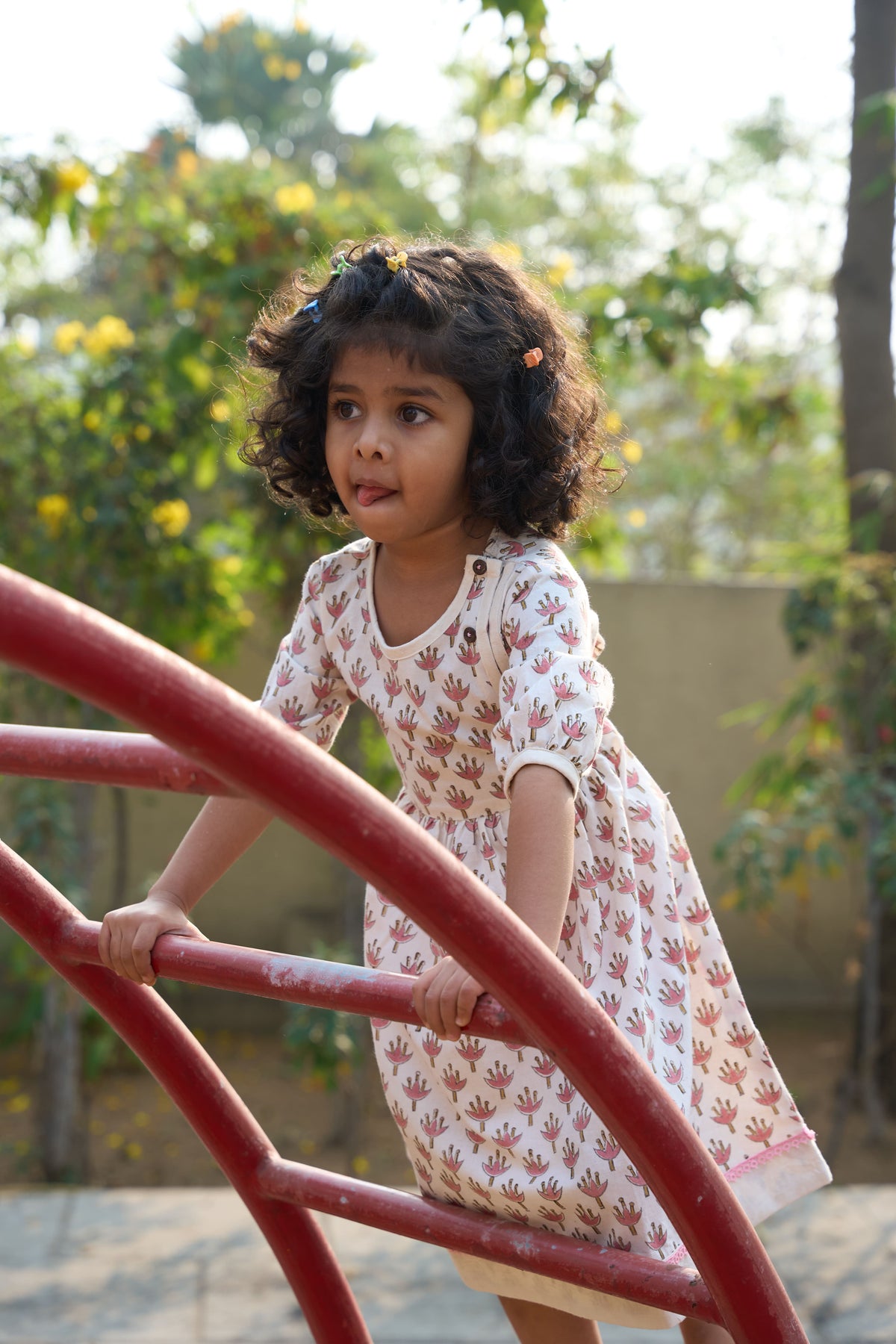 Young girl in a floral dress standing on a playground with greenery in the background