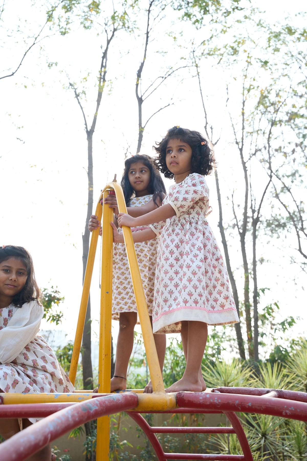 Three young girls playing on a playground structure with trees in the background