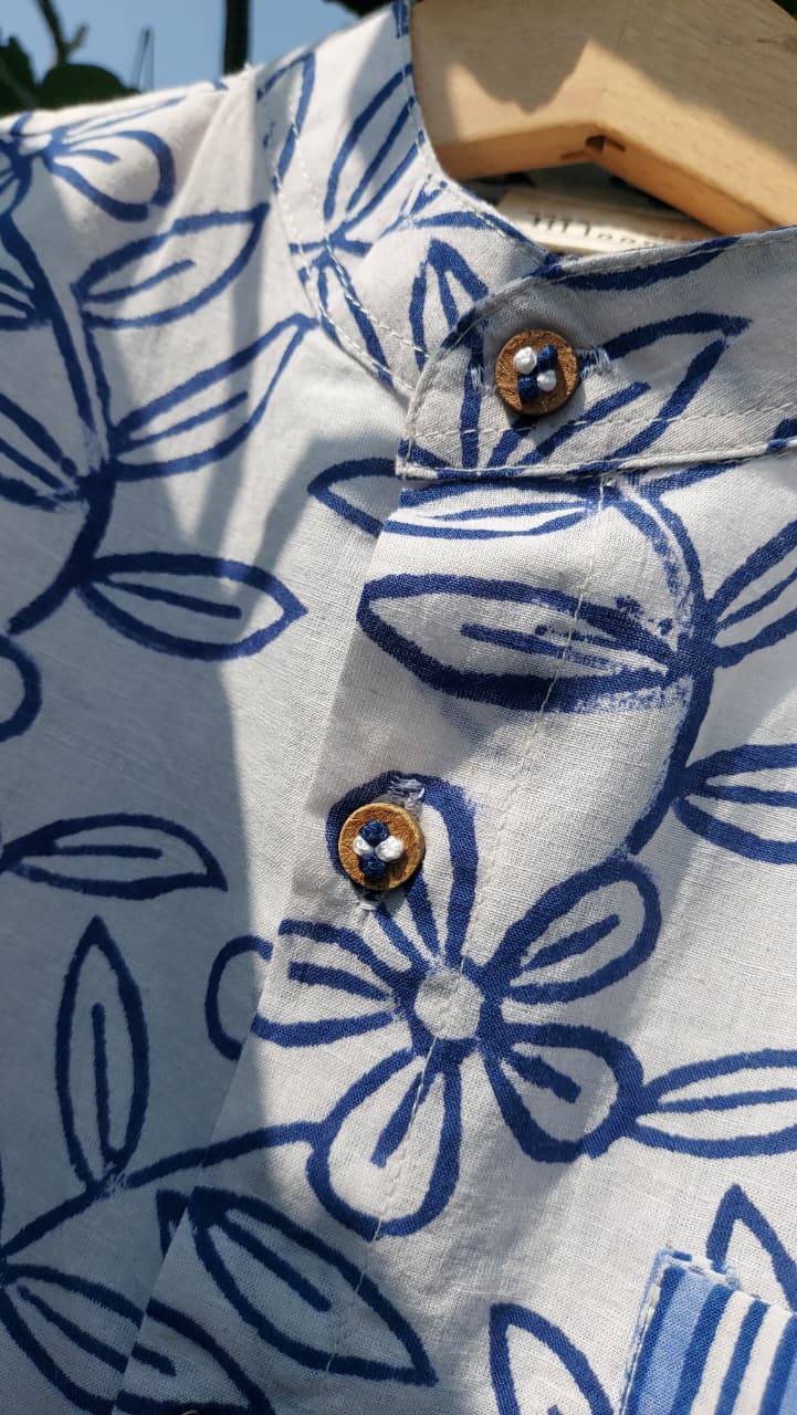 Close-up of a white cotton shirt with a blue floral block print pattern, featuring a mandarin collar and decorative wooden buttons.