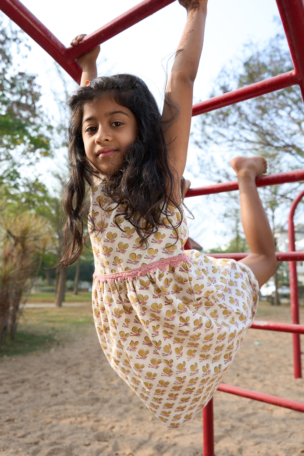 Young girl in a floral dress hanging from playground equipment