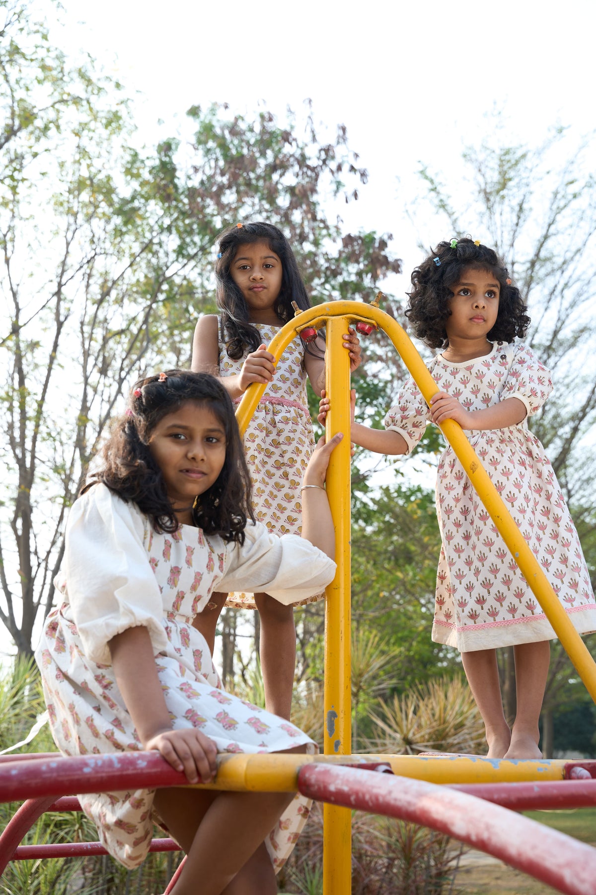 Three young girls playing on a playground structure with trees in the background