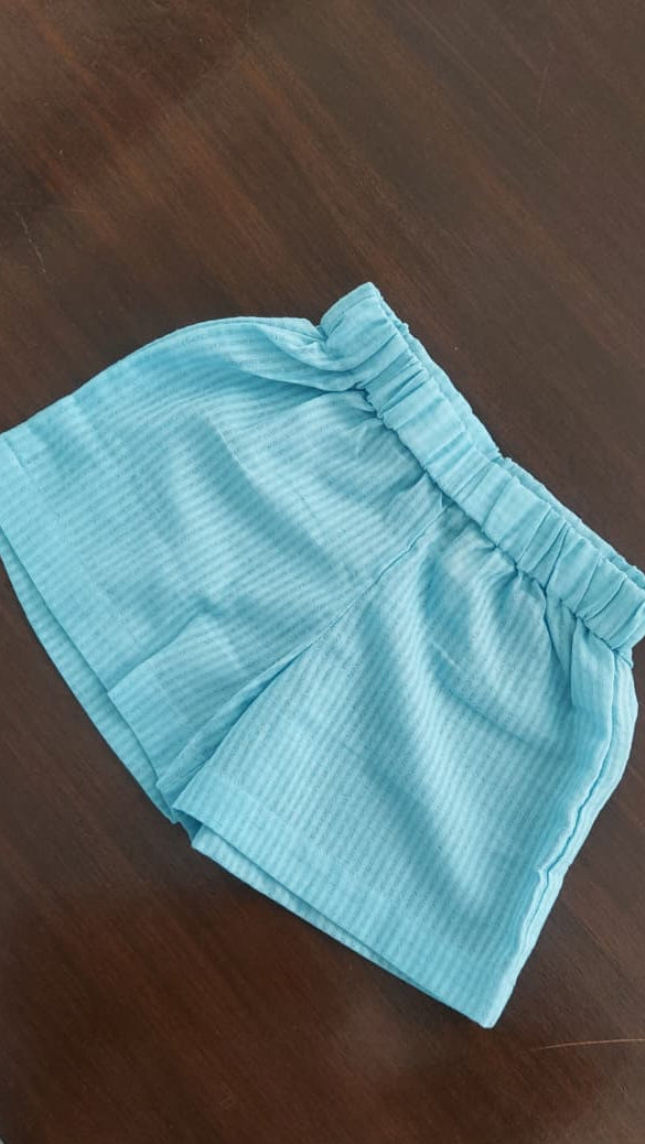Light blue striped shorts with an elastic waistband, laid flat on a dark brown wooden floor.
