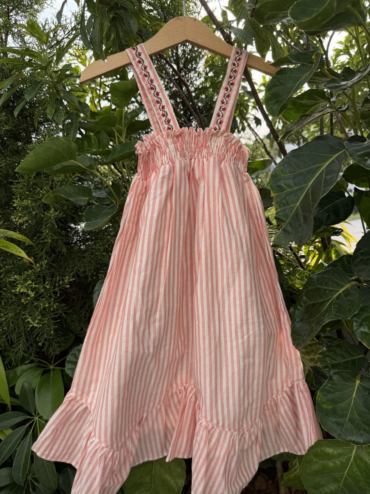 Pink striped dress on a hanger against a green leafy background