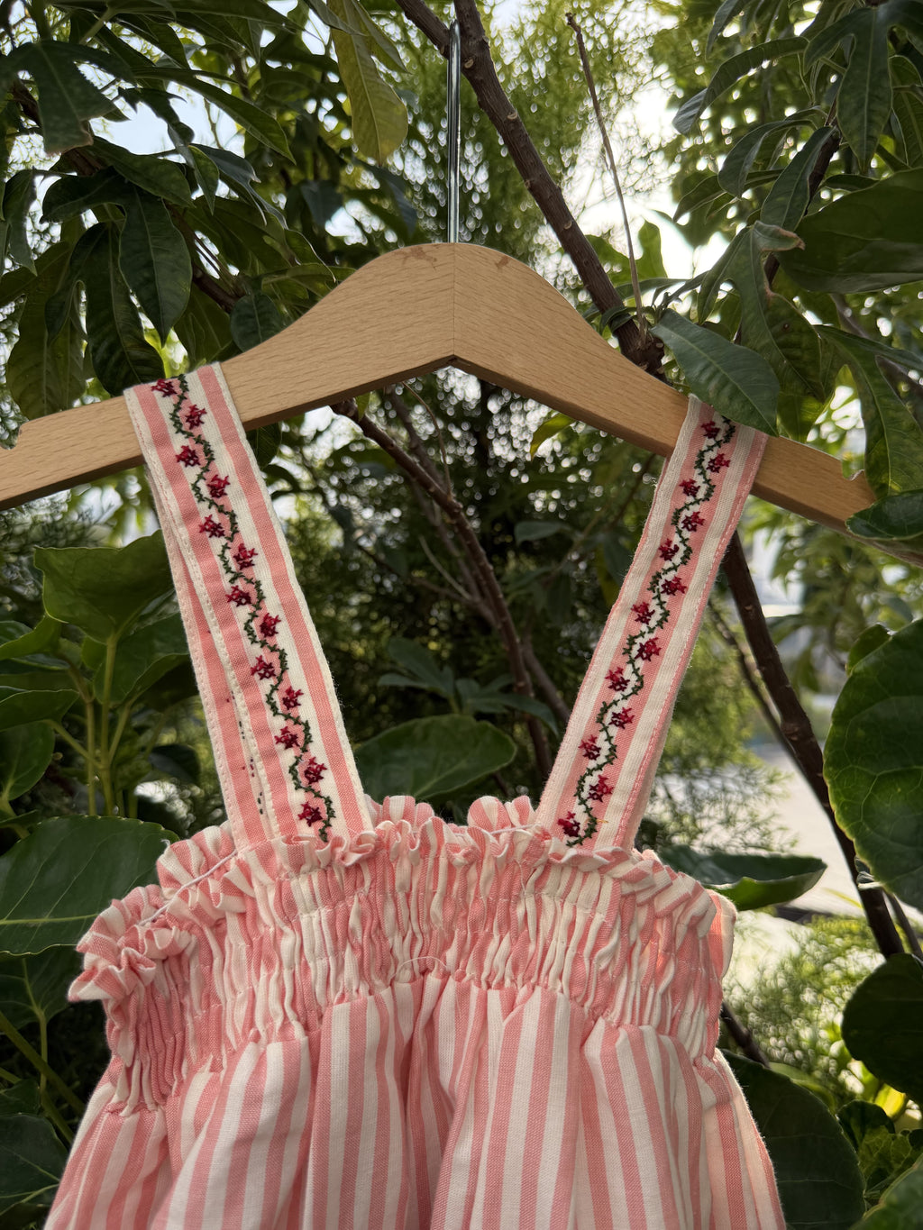 Pink dress with floral embroidery on a hanger against a green leafy background