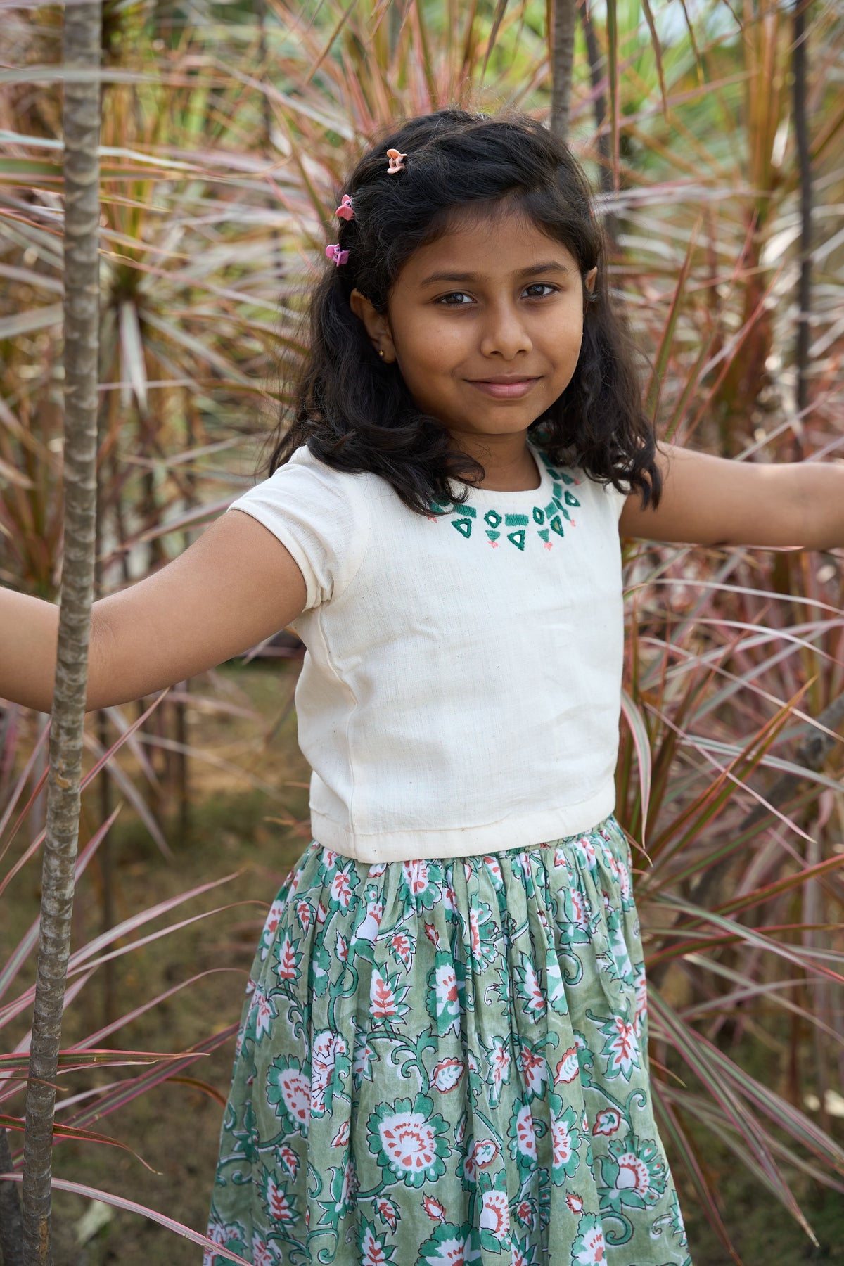 Young girl in a white top and floral skirt standing among plants