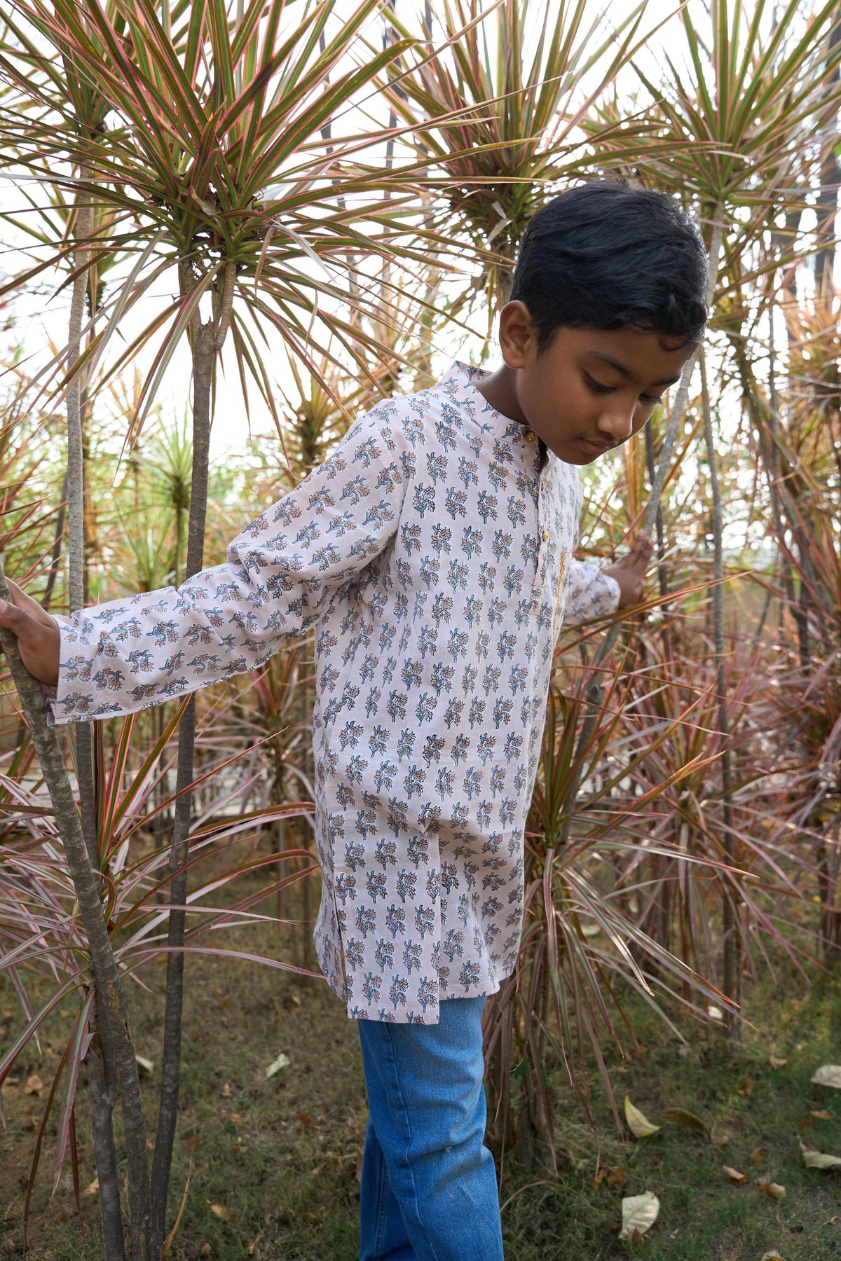Child in a patterned shirt and blue pants standing among tall plants