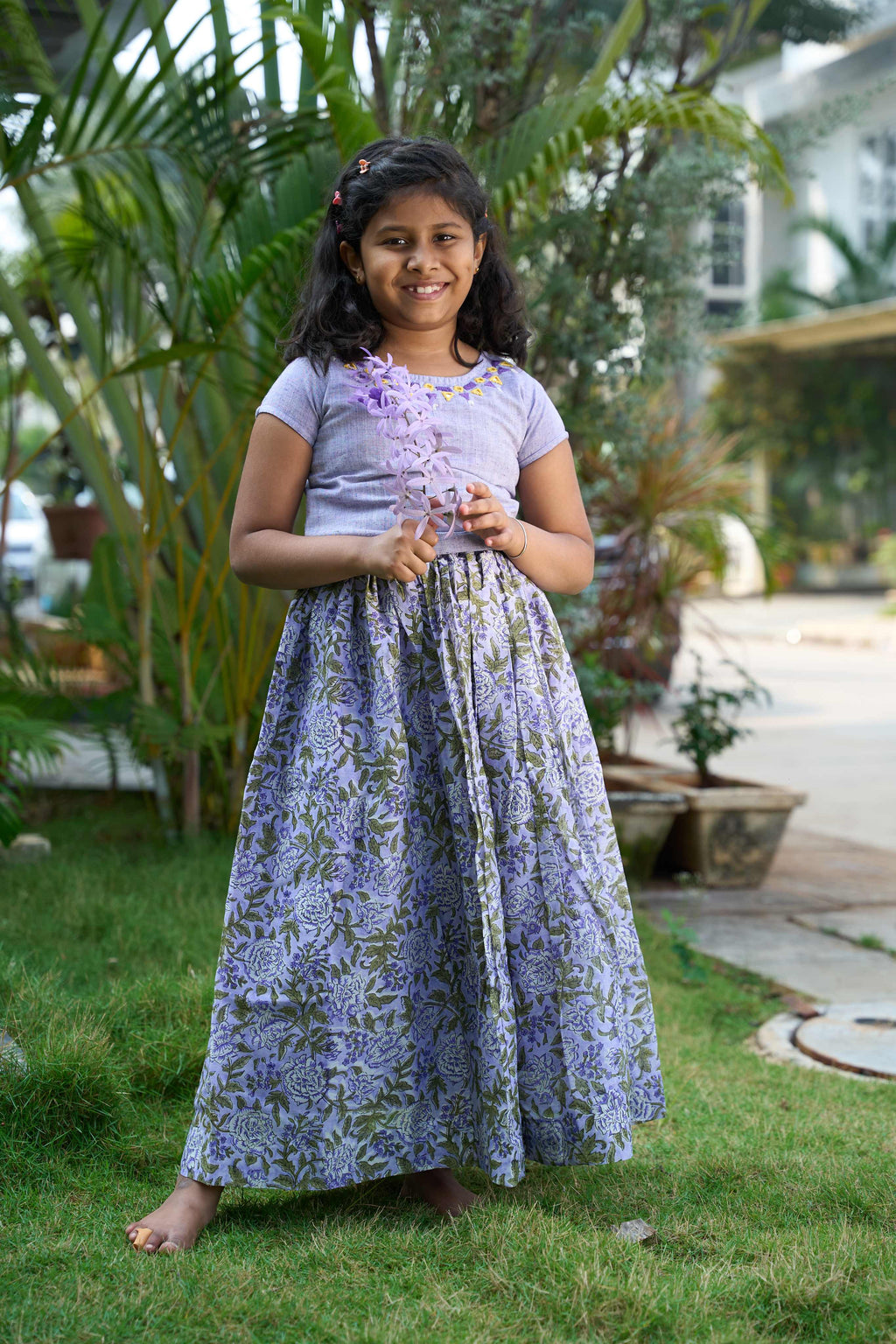 Young girl in a garden wearing a floral dress and holding flowers.