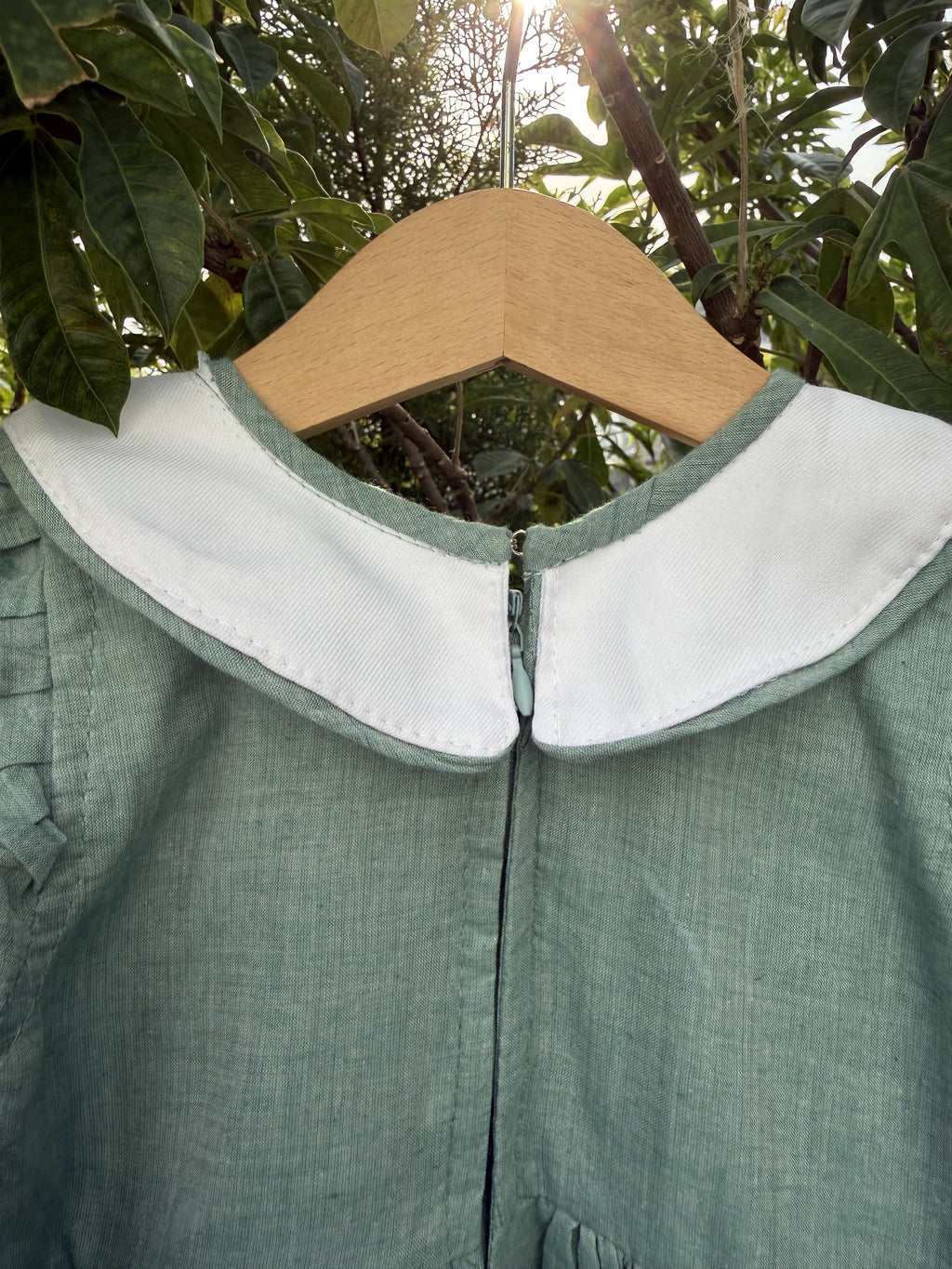 Green dress with white lining on a hanger against a leafy background