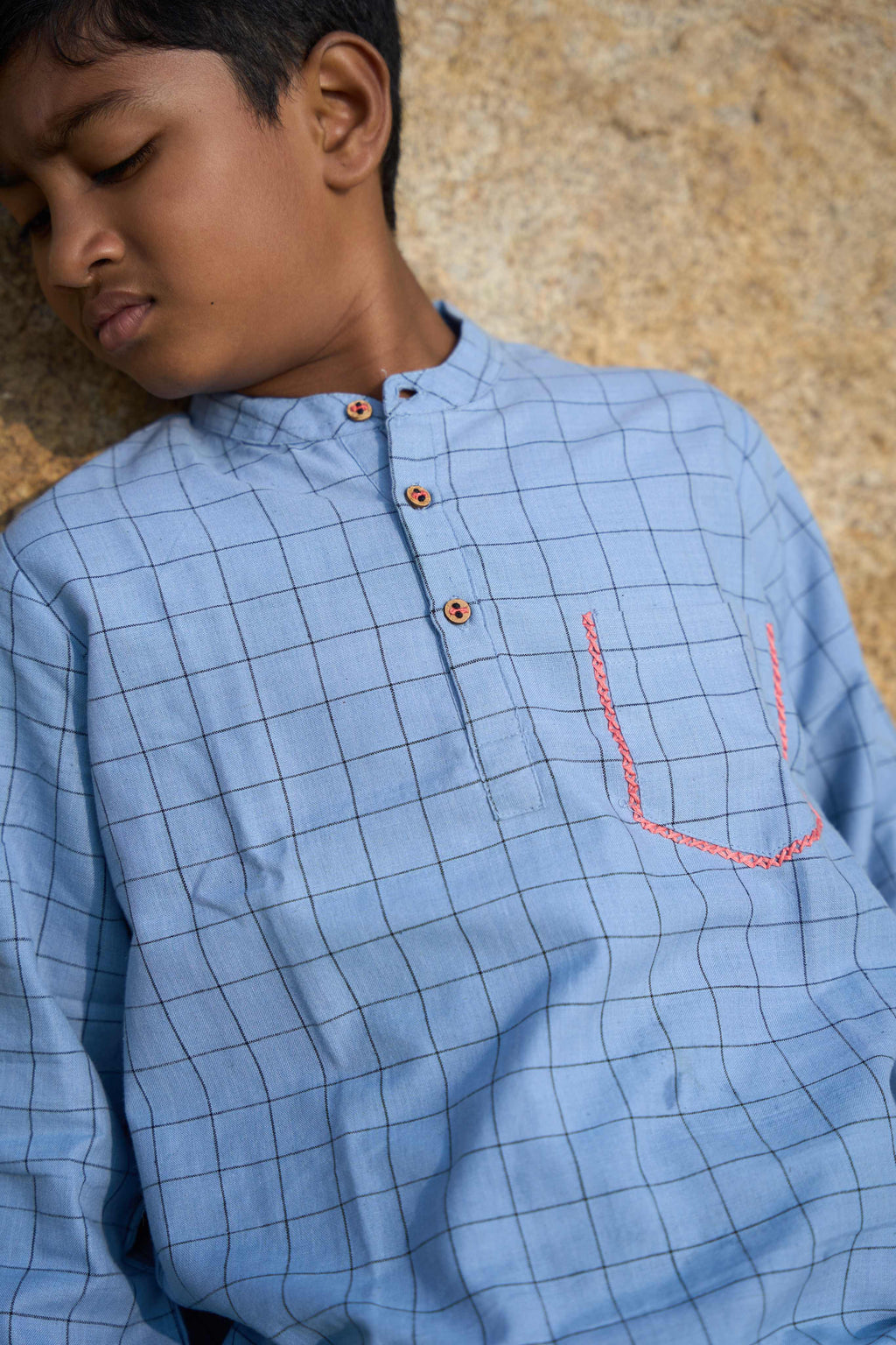 Child wearing a blue checkered shirt with a textured beige background