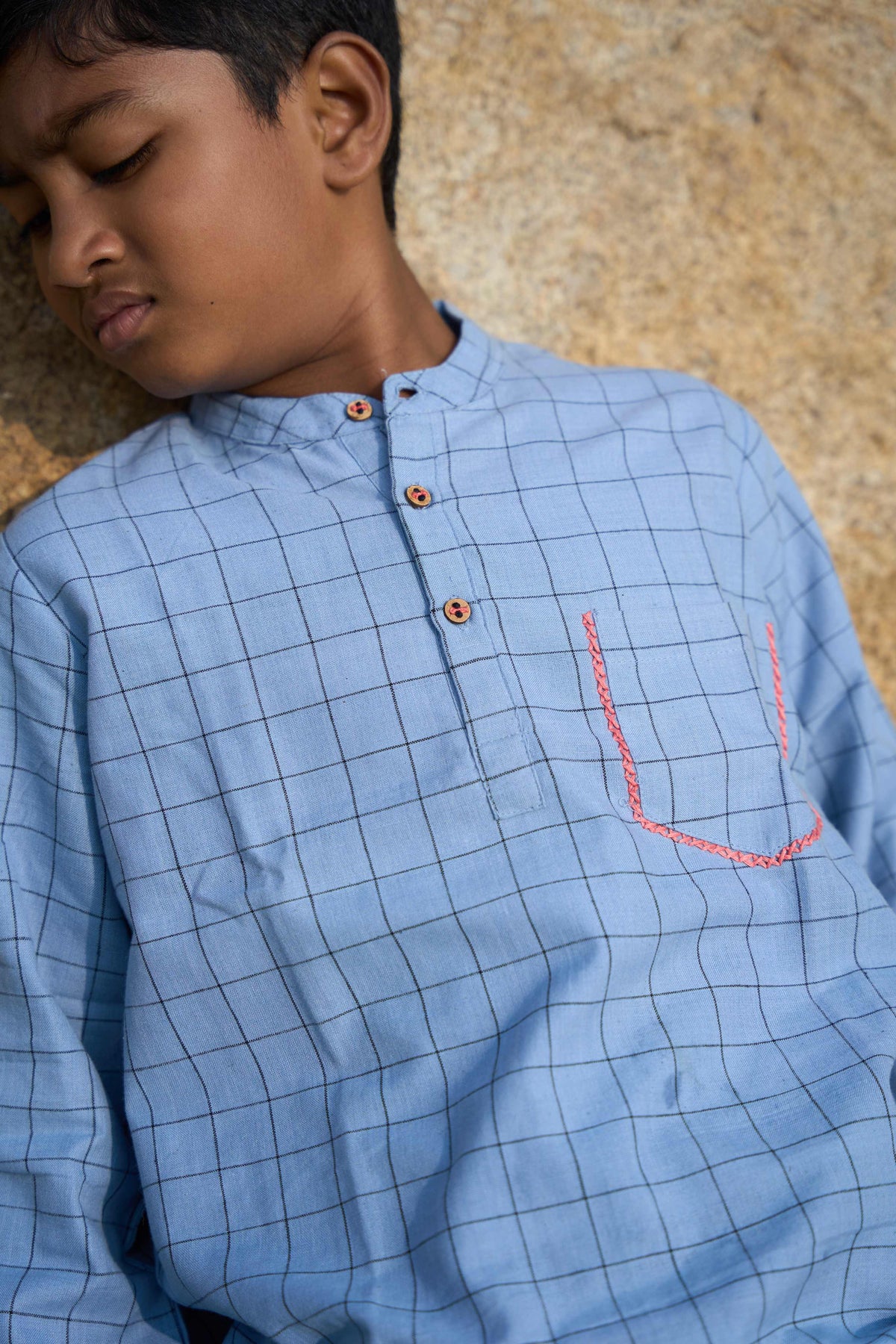 Child wearing a blue checkered shirt with a textured beige background