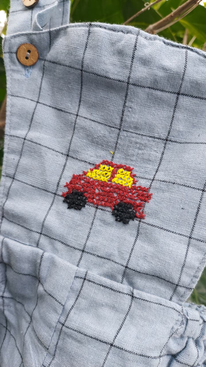 Close-up of a Grey khadi  with a black grid pattern, featuring a small cross stitch embroidered red car with yellow windows on the chest.