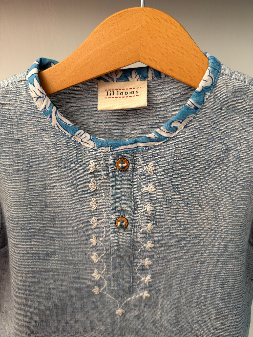 Close-up of a denim shirt with embroidery and a brown patch on a neutral background