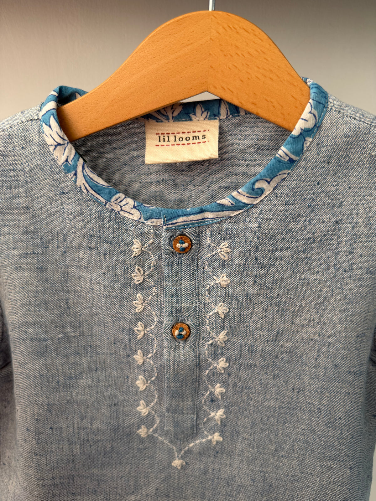 Close-up of a denim shirt with embroidery and a brown patch on a neutral background