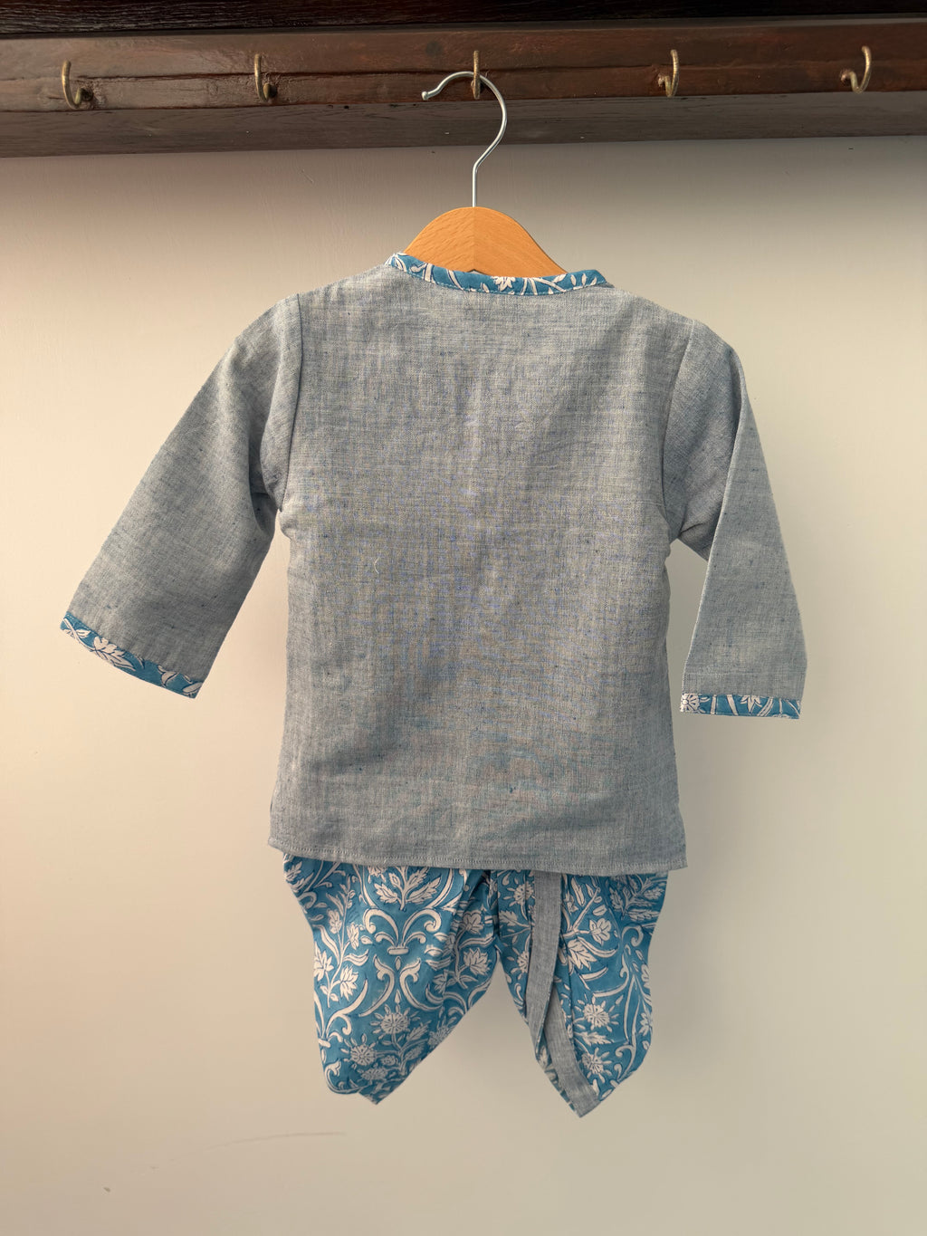 Gray shirt with blue floral cuffs and hem on a hanger against a white wall