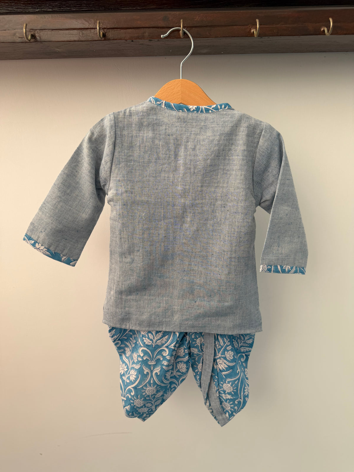 Gray shirt with blue floral cuffs and hem on a hanger against a white wall