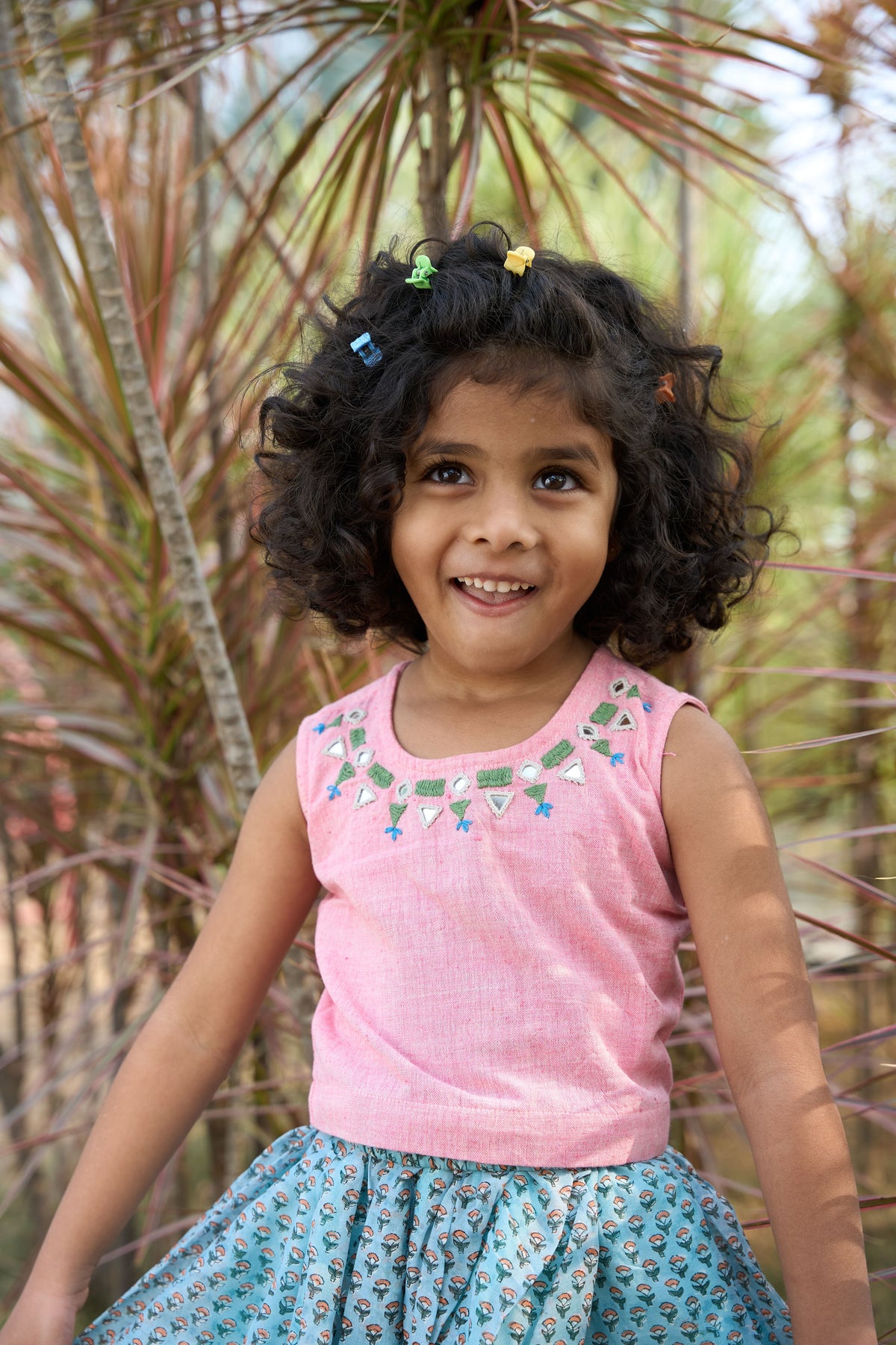 Young girl in a pink top and blue skirt standing in front of plants