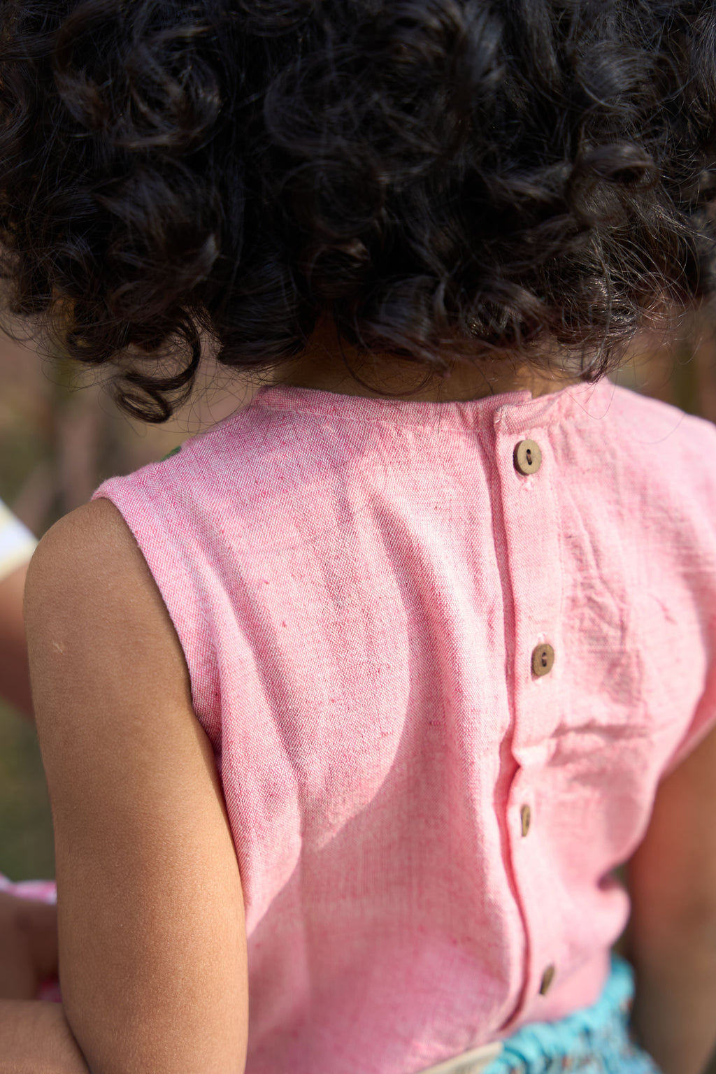 Person wearing a pink sleeveless shirt with buttons, blurred background