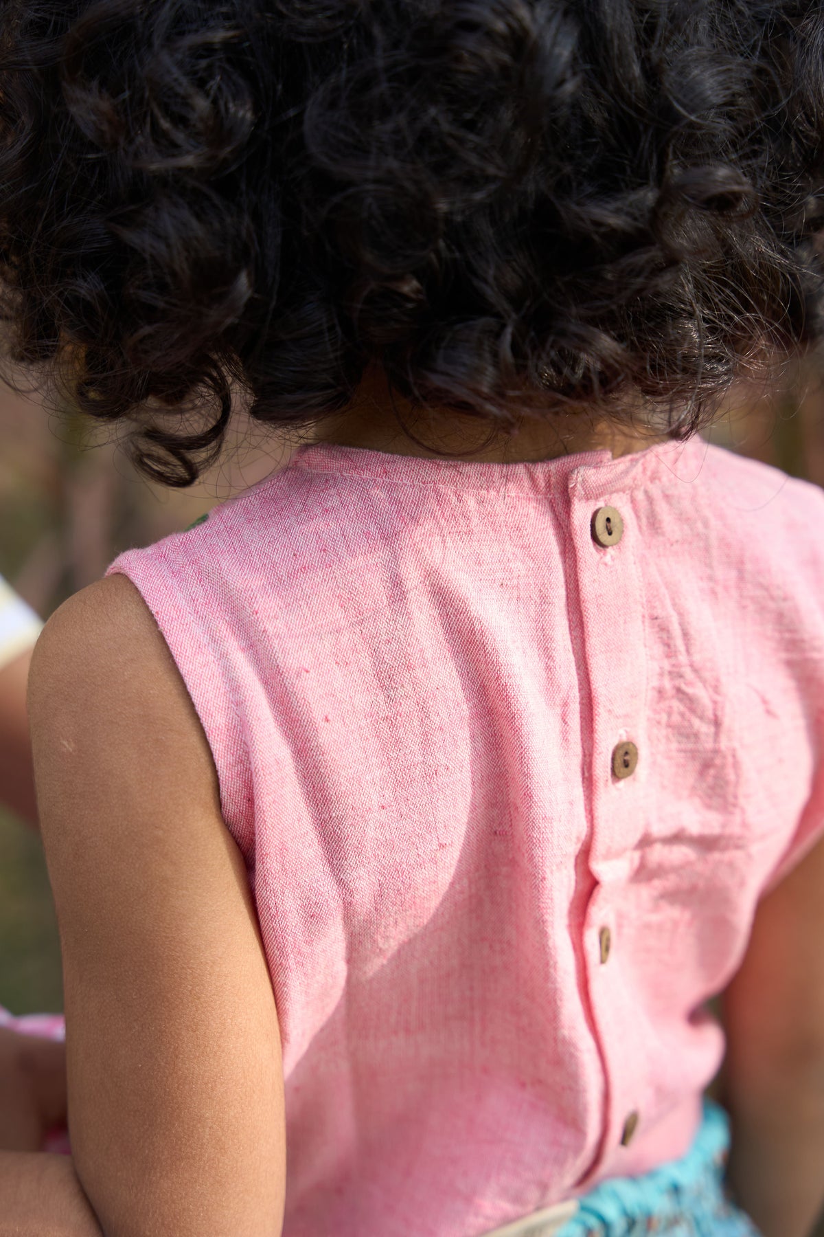 Person wearing a pink sleeveless shirt with buttons, blurred background
