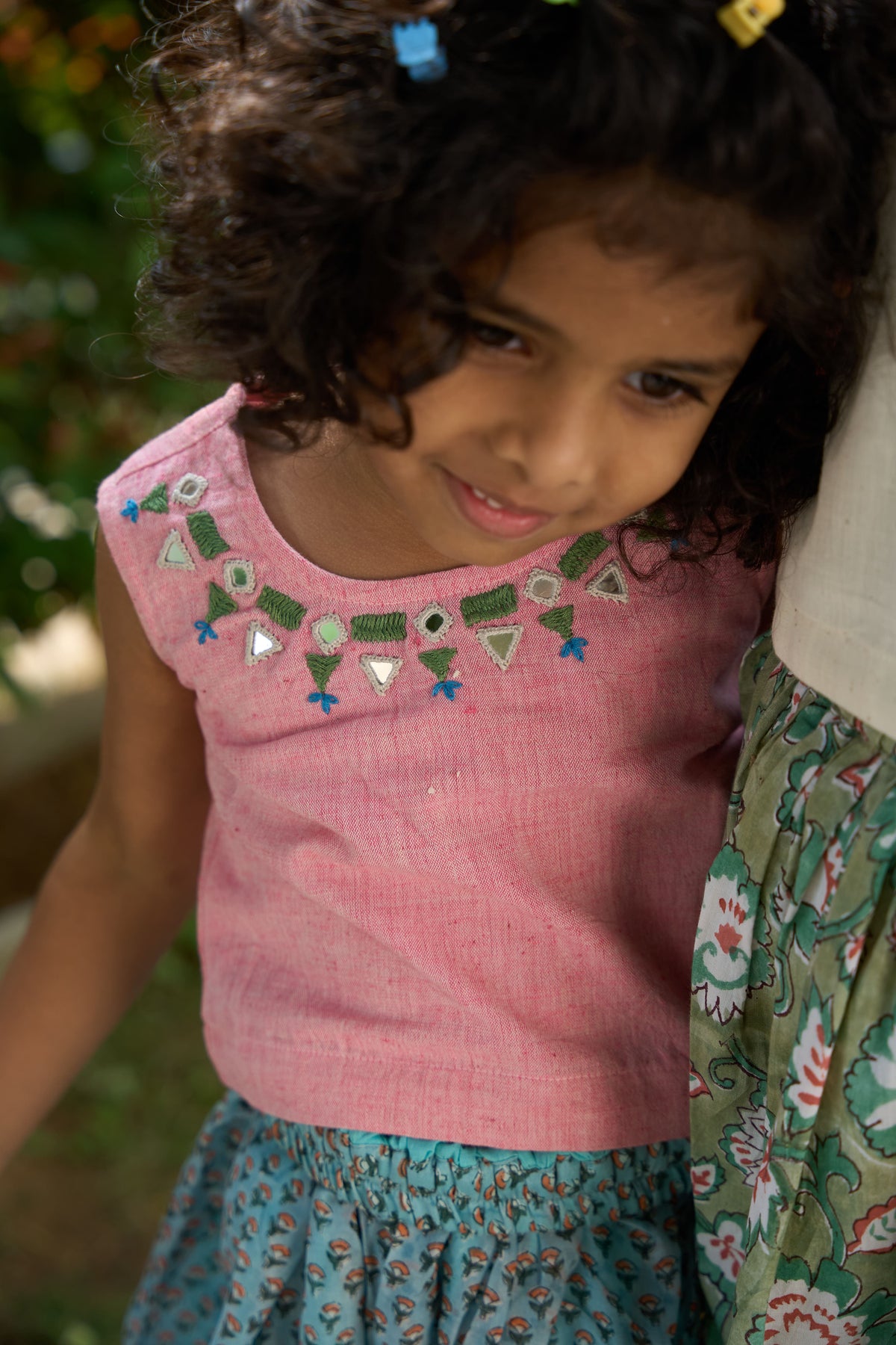 Young girl wearing a pink top with decorative patterns and a floral skirt.