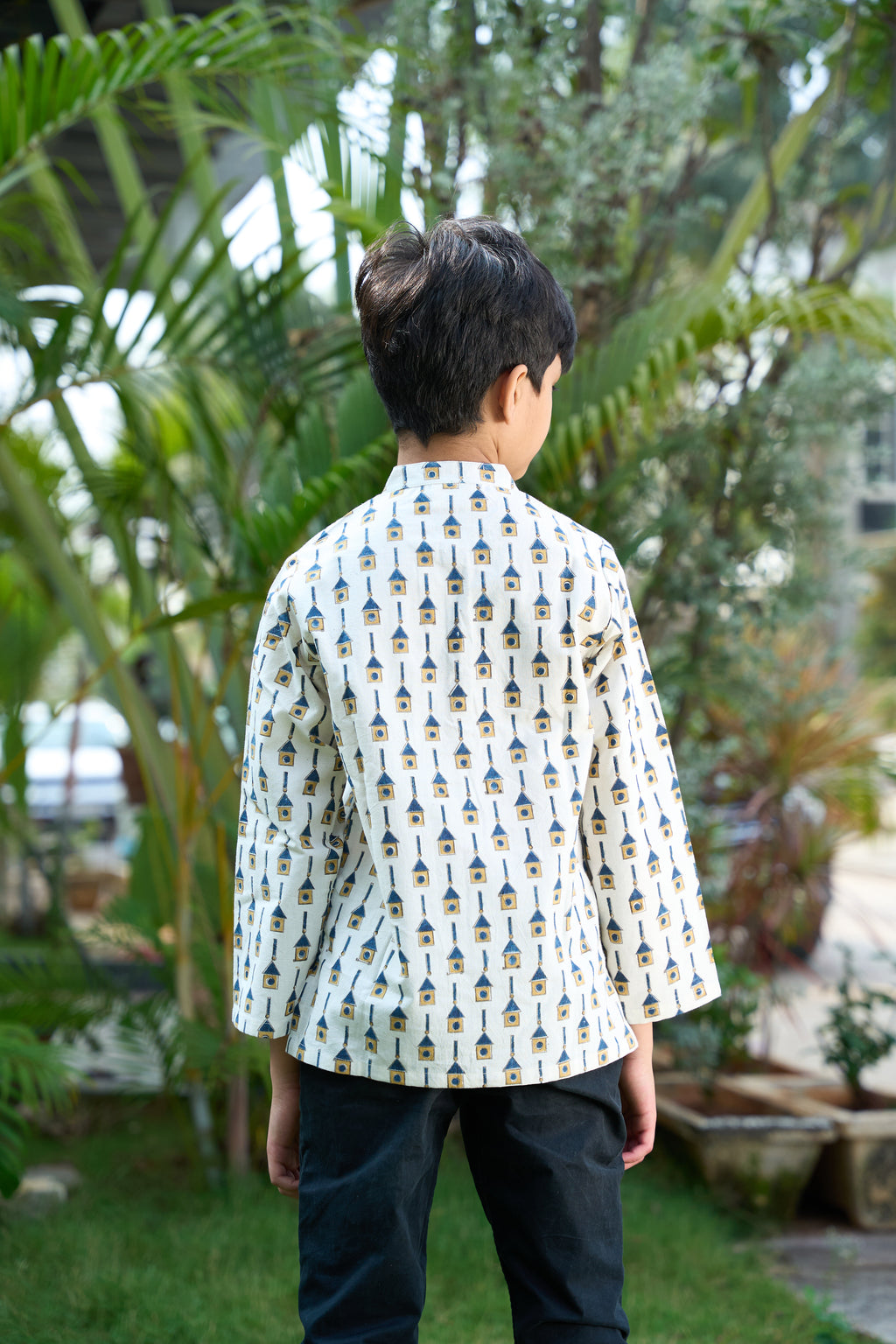 Child wearing a patterned shirt standing in a garden with greenery
