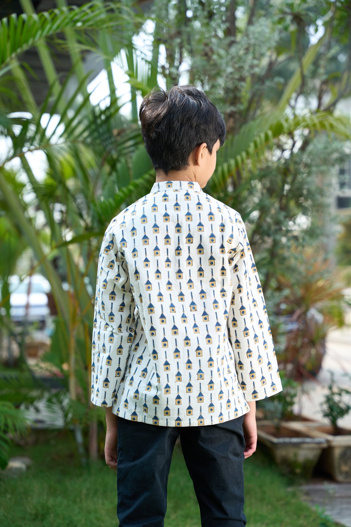 Child wearing a patterned shirt standing in a garden with greenery