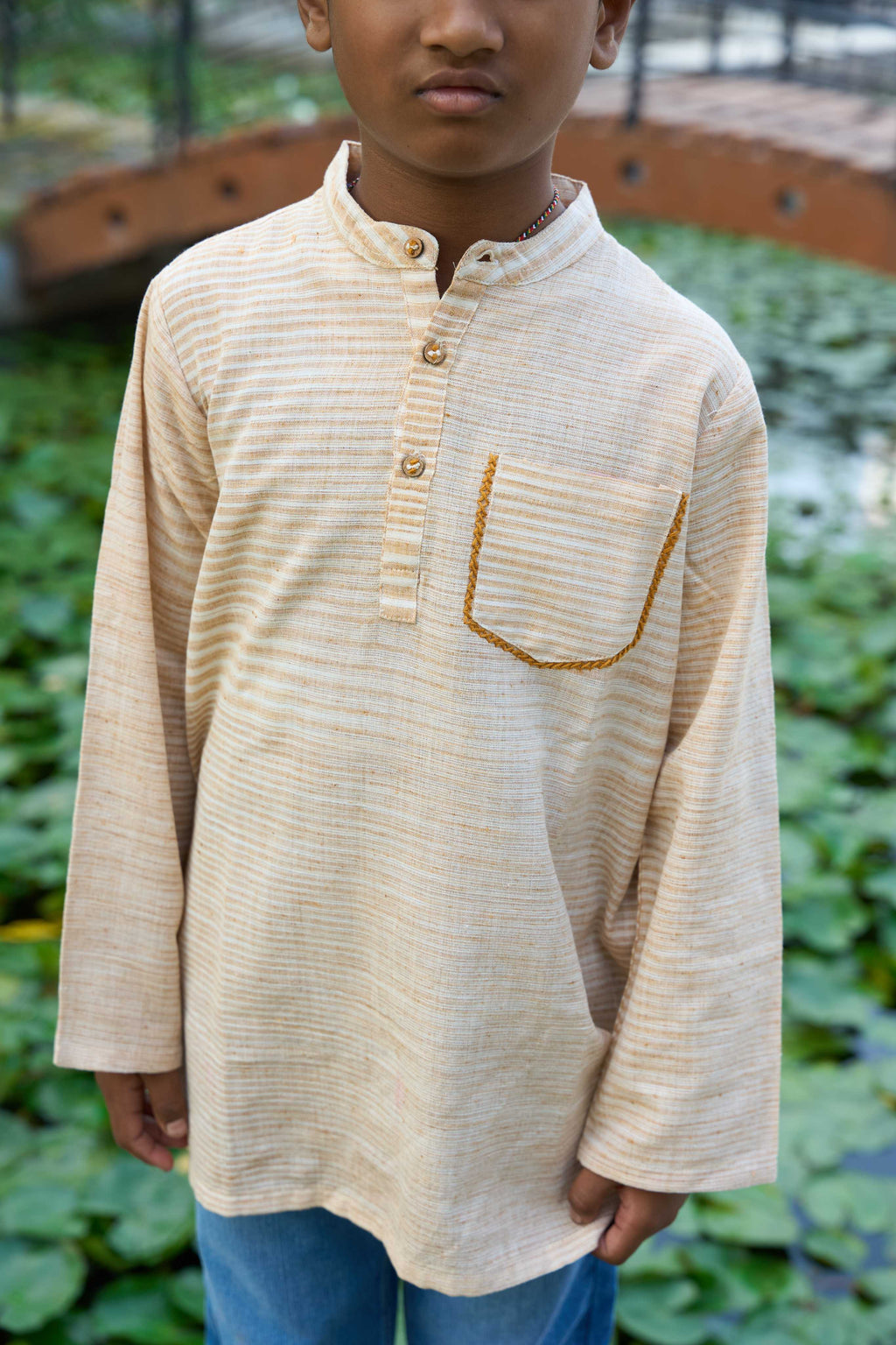 Child wearing a beige long-sleeve shirt with a pocket in an outdoor setting
