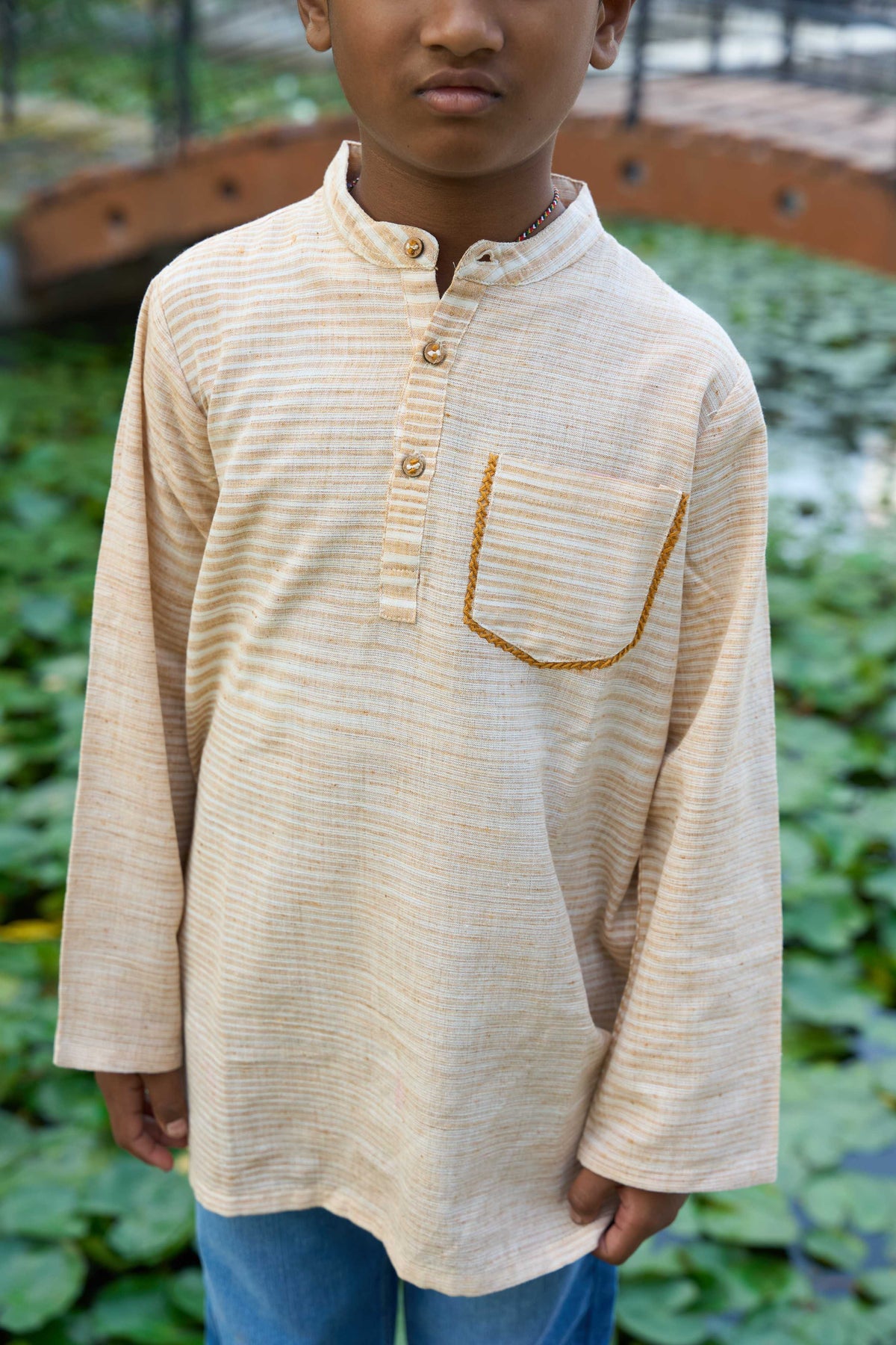 Child wearing a beige long-sleeve shirt with a pocket in an outdoor setting