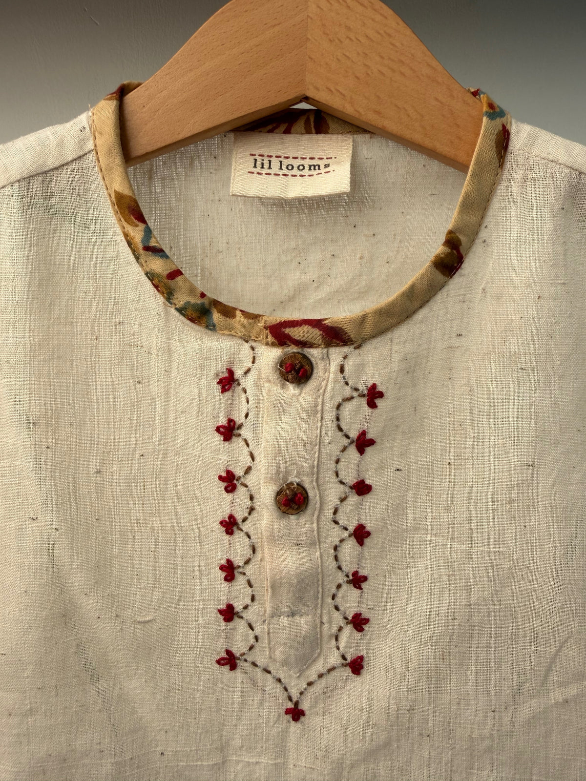 Close-up of a beige garment with floral embroidery on a hanger, featuring a label.