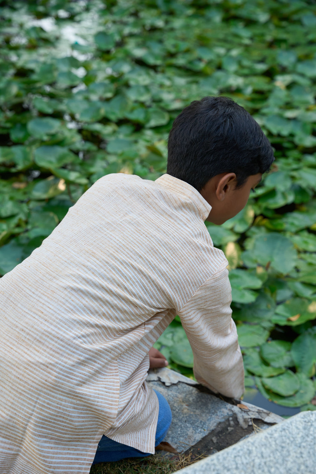 Person in a beige shirt and blue pants crouching near green foliage