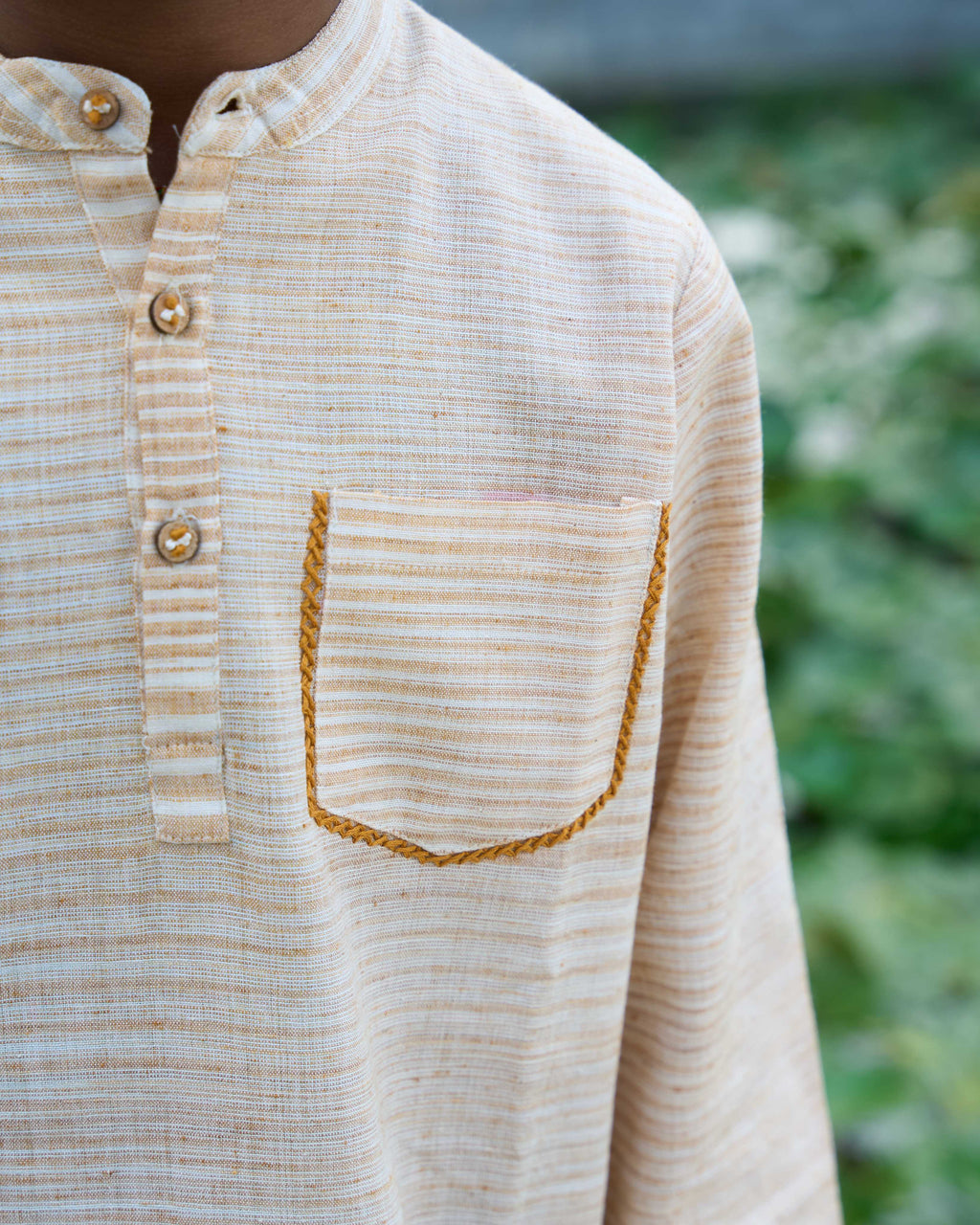 Close-up of a beige button-up shirt with a pocket against a blurred green background