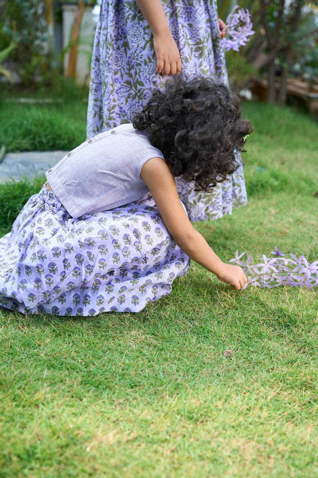 Two children in matching floral dresses playing in a garden.