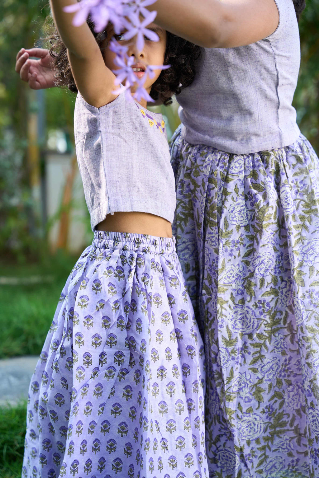 Two people wearing matching purple floral skirts outdoors.