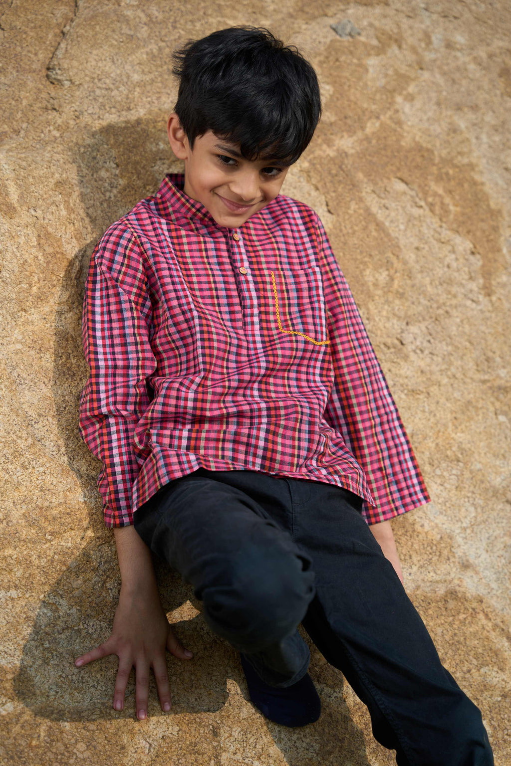 Child wearing a red and black checkered shirt sitting on a stone surface