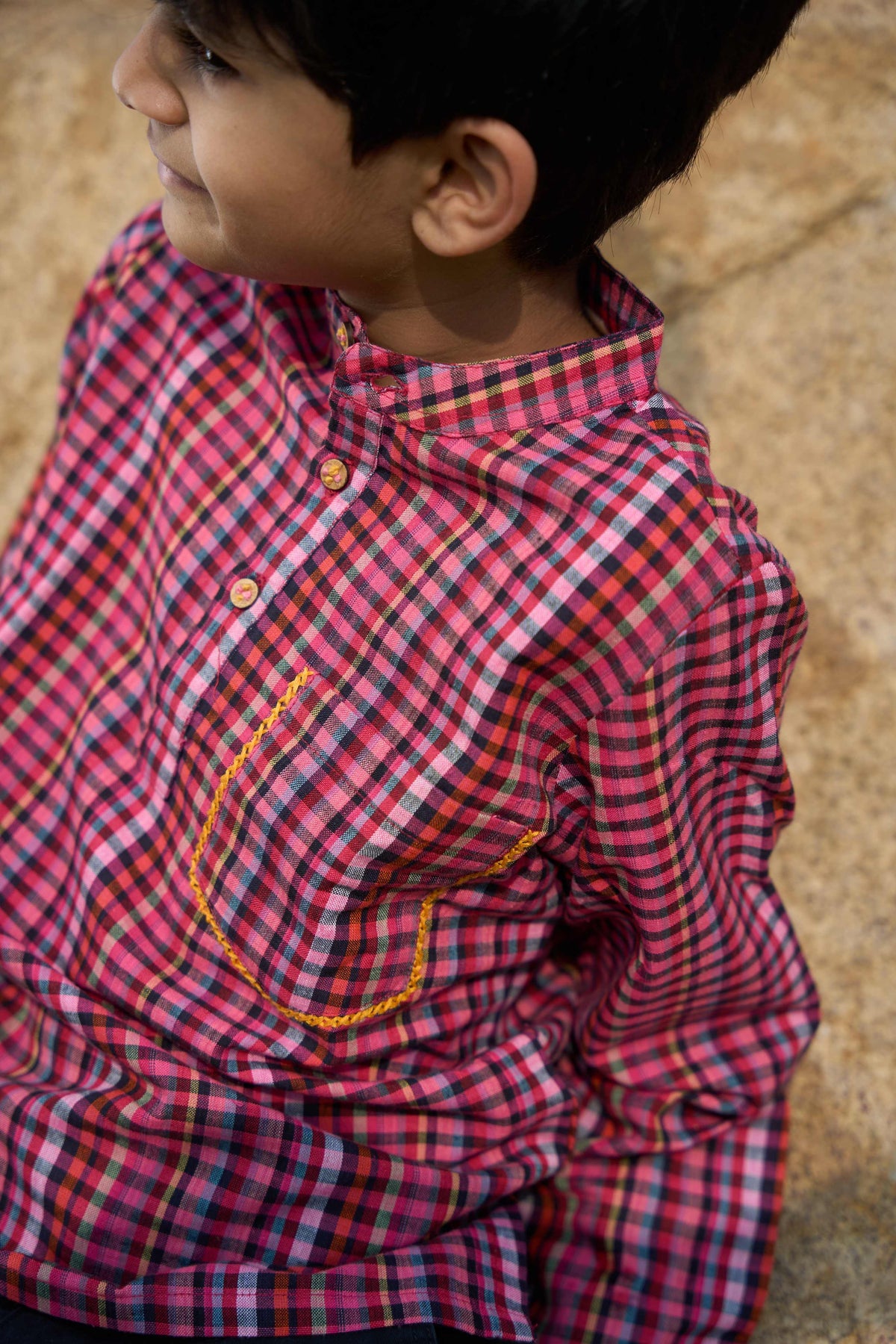 Child wearing a red and blue checkered shirt on a textured surface