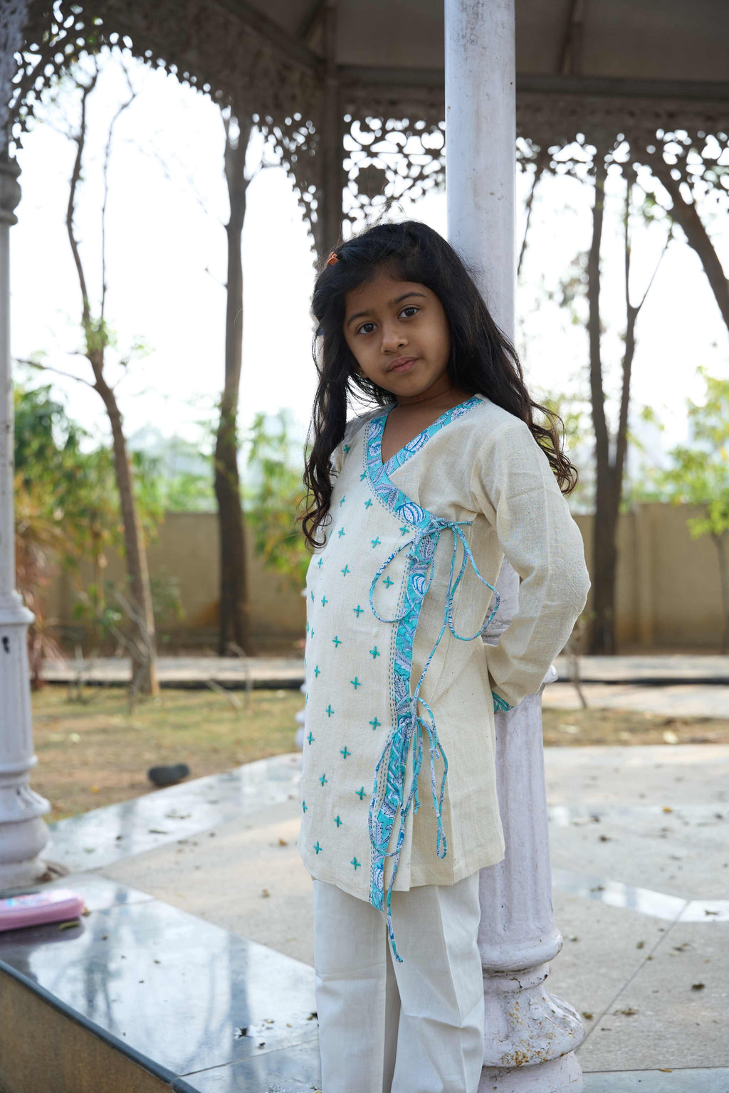 Young girl in a white and blue traditional outfit standing under a decorative archway.