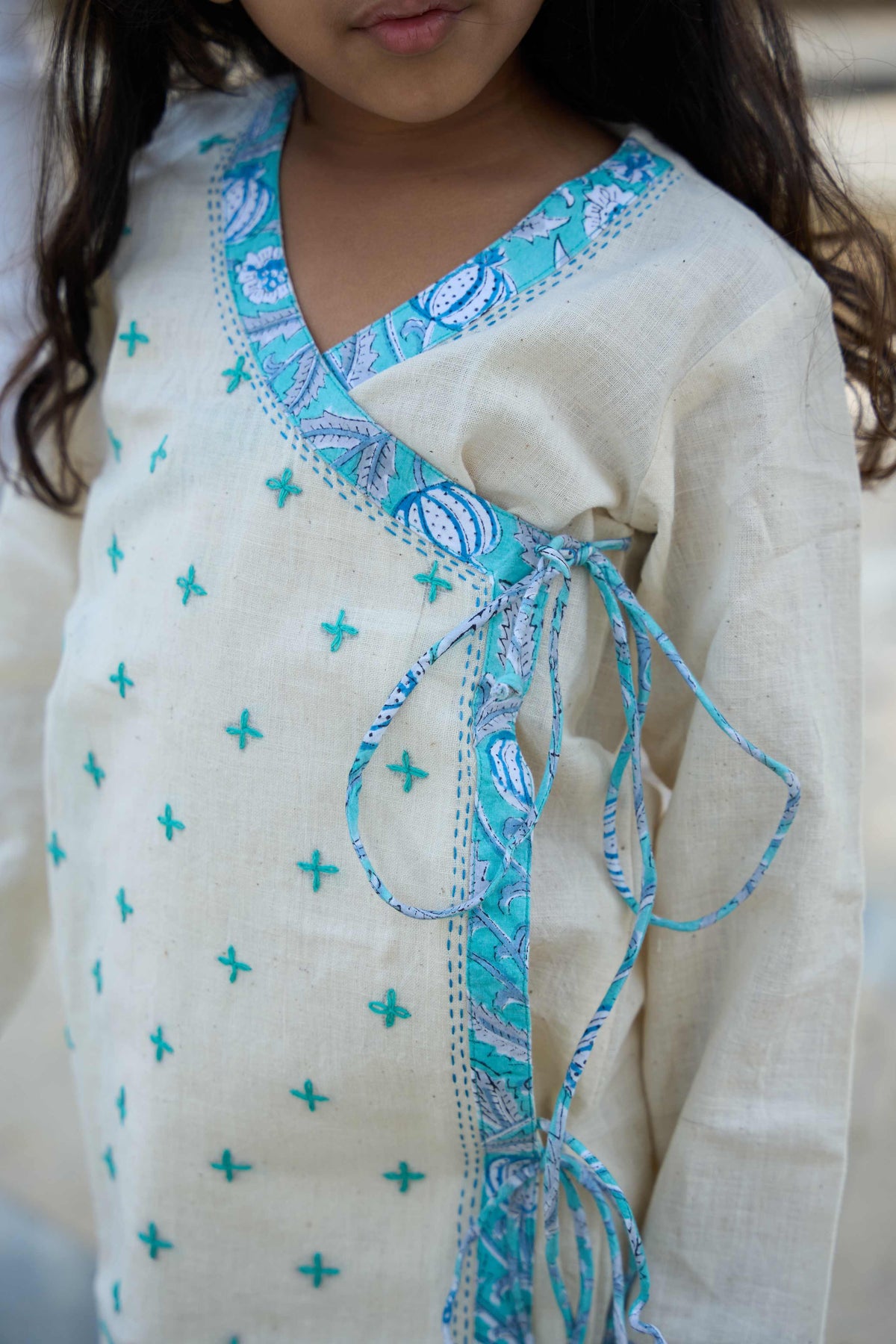 Child wearing a cream-colored outfit with blue patterns and embroidery.