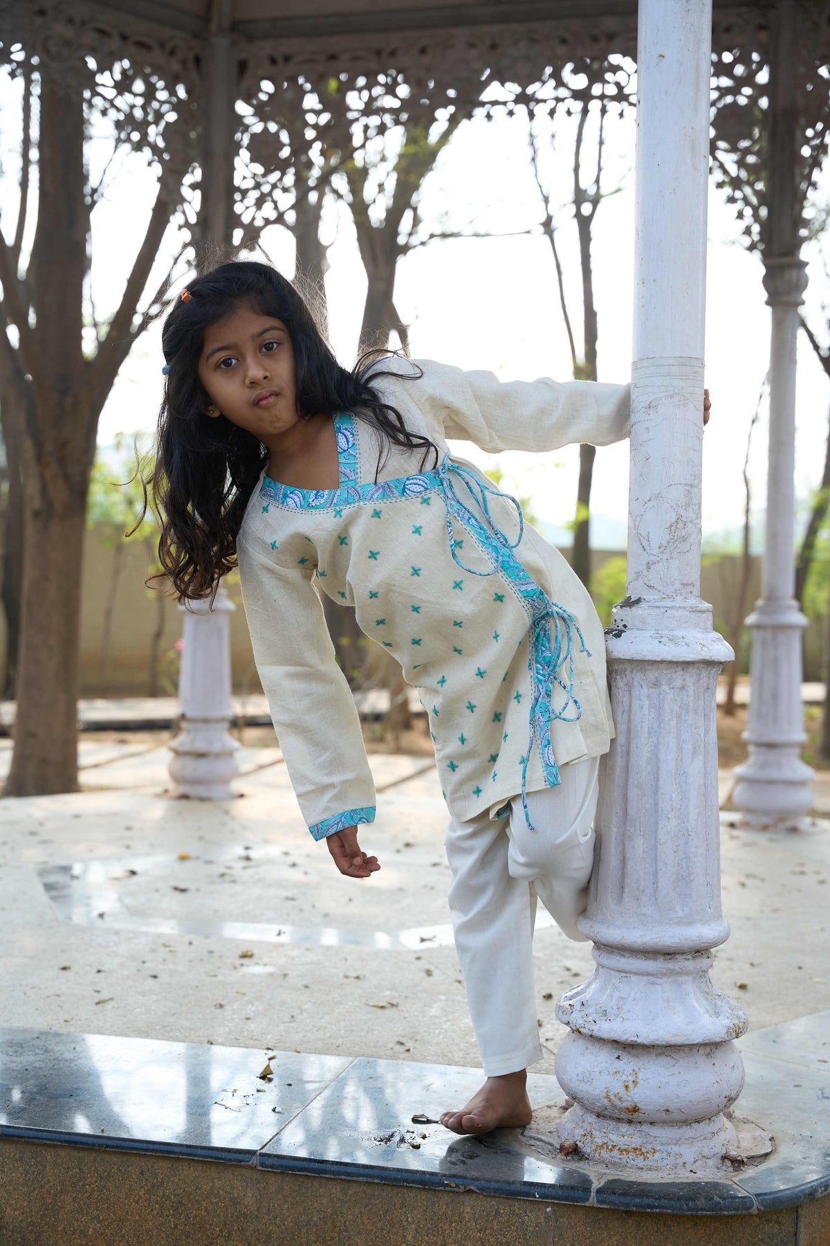 Young girl in a traditional outfit standing on a stone platform with trees in the background