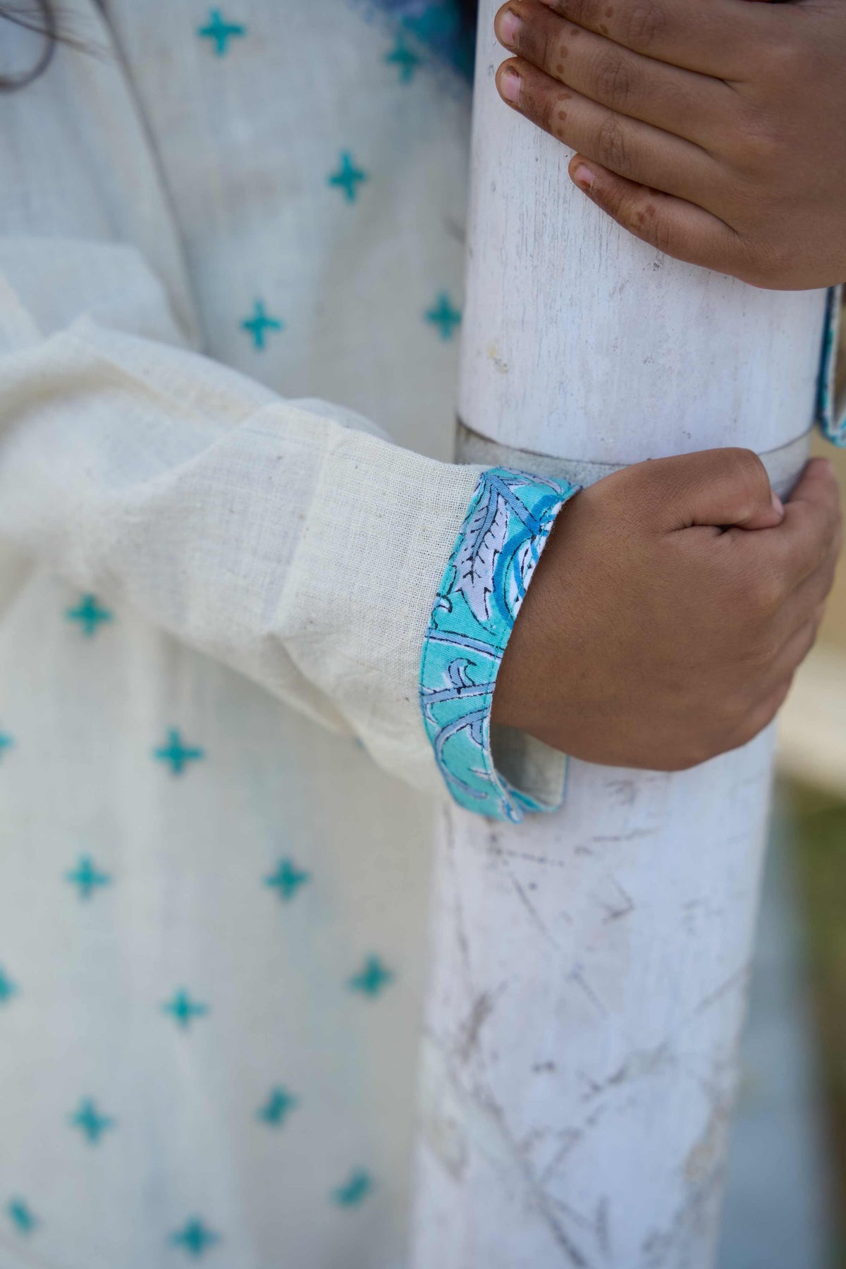 Close-up of a person wearing a white garment with blue patterns, holding a cylindrical object.