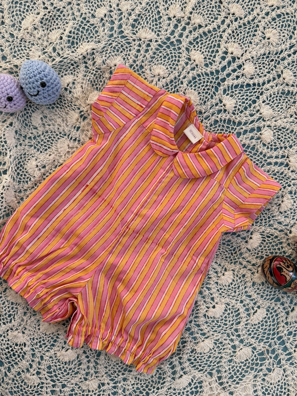 Pink and yellow striped baby romper on a textured surface