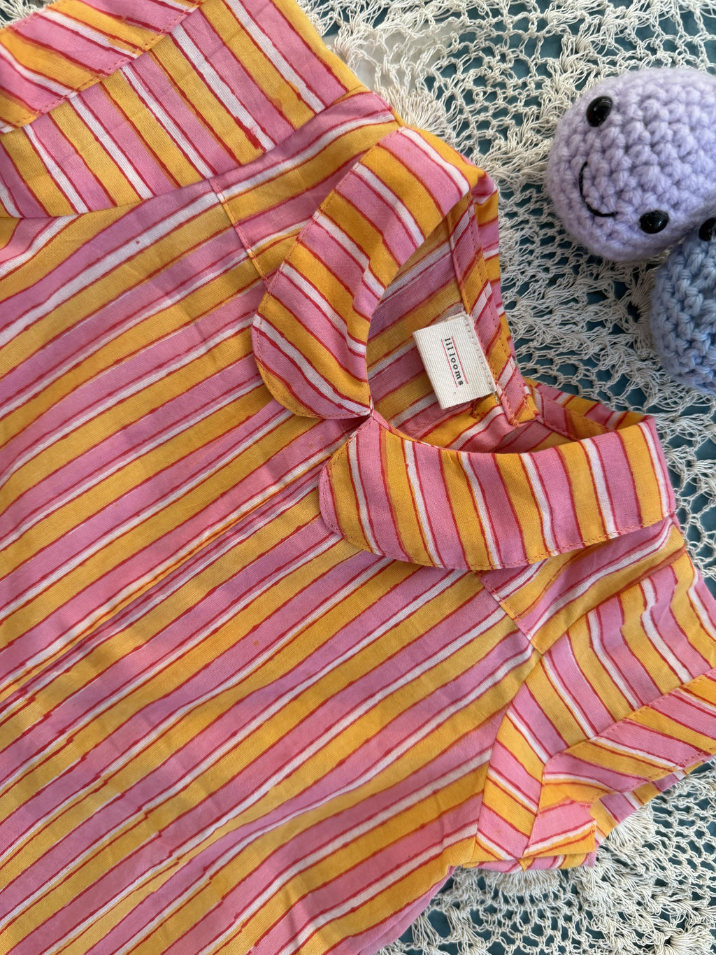 Pink and yellow striped dress with a small toy in the background