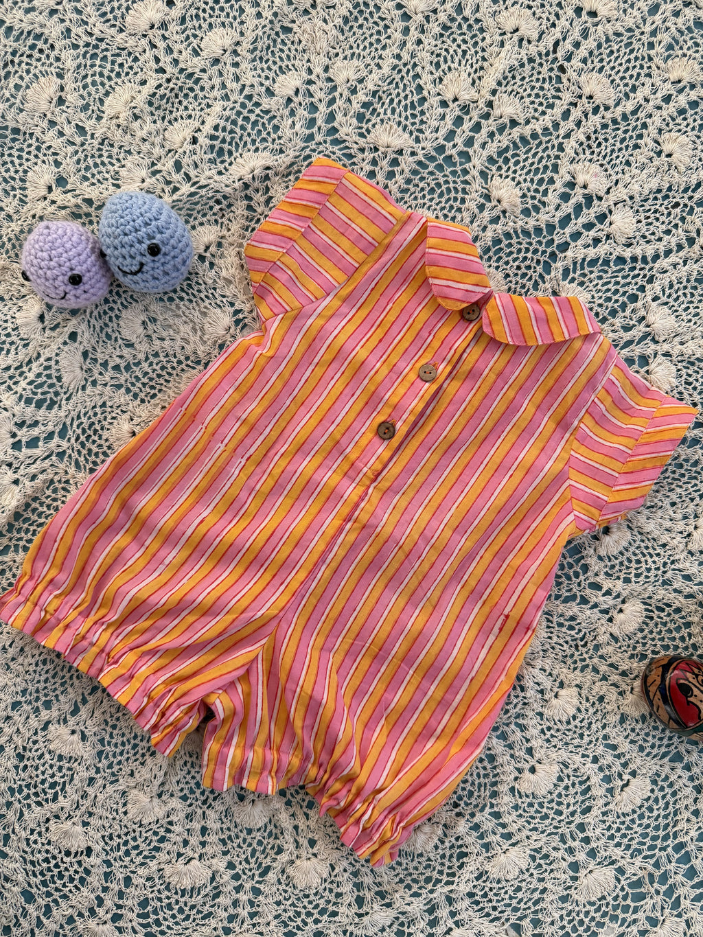 Pink and yellow striped baby romper on a textured surface with small toys.