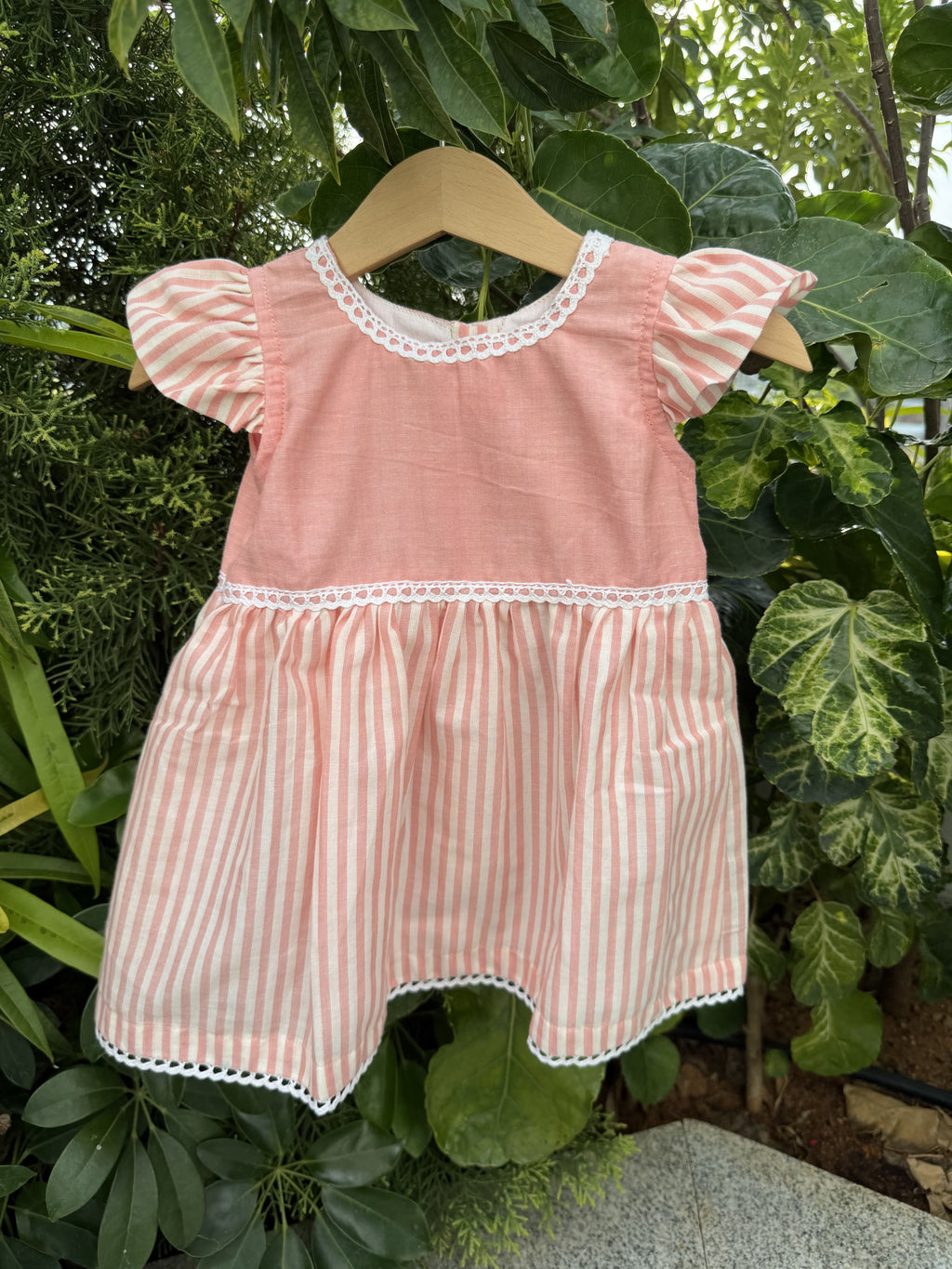 Pink and white striped dress on a hanger against a green leafy background