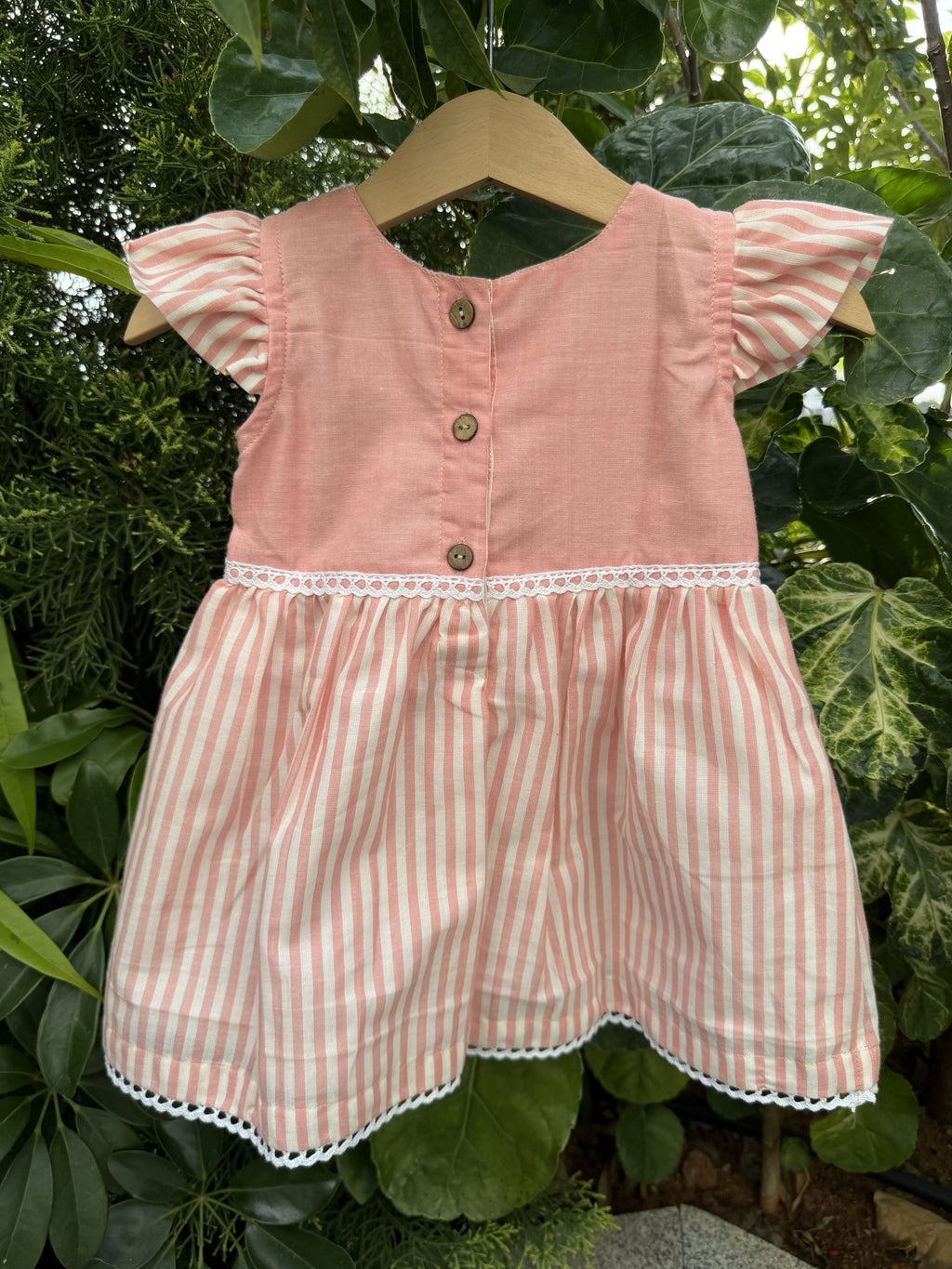 Pink and white striped dress with ruffled details on a green leafy background
