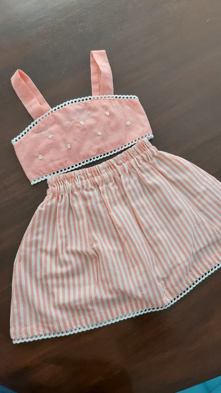 A baby girl's two-piece outfit consisting of a pink and white striped romper and a matching pink bodysuit, laid flat on a dark wooden surface.