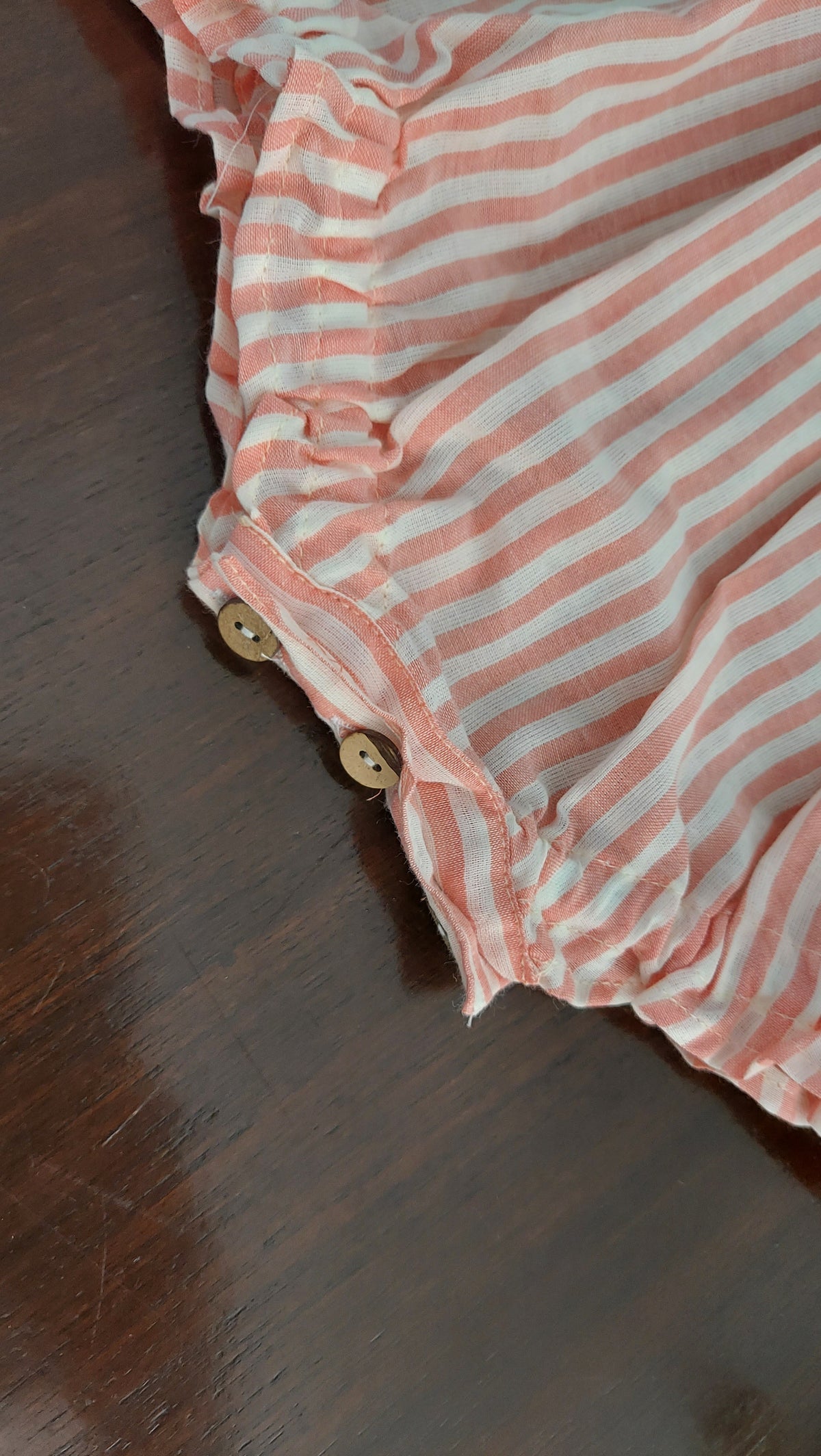 Pink and white striped fabric with buttons on a wooden surface