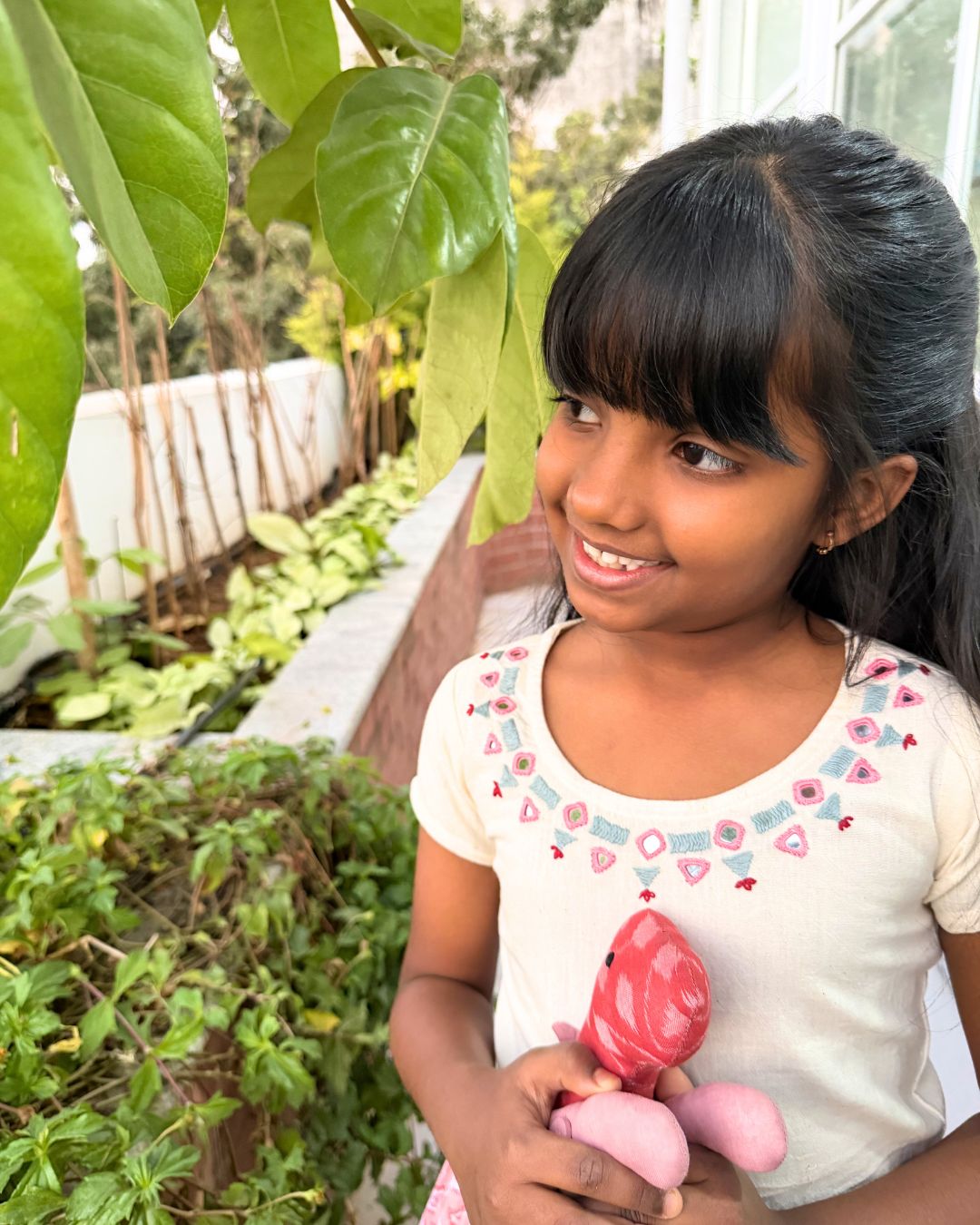 Young girl holding a pink toy in a garden setting