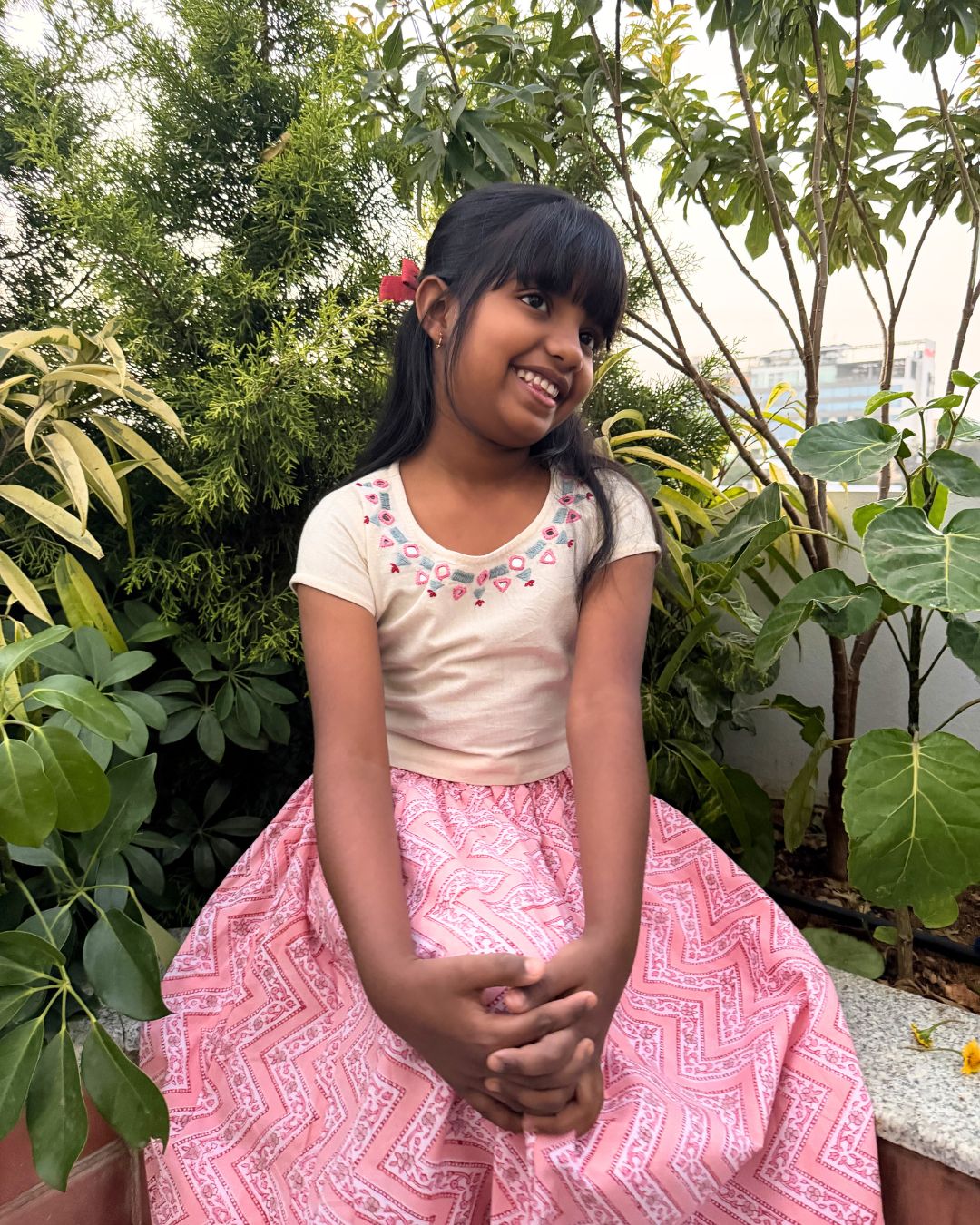 Young girl in a pink skirt sitting among green plants