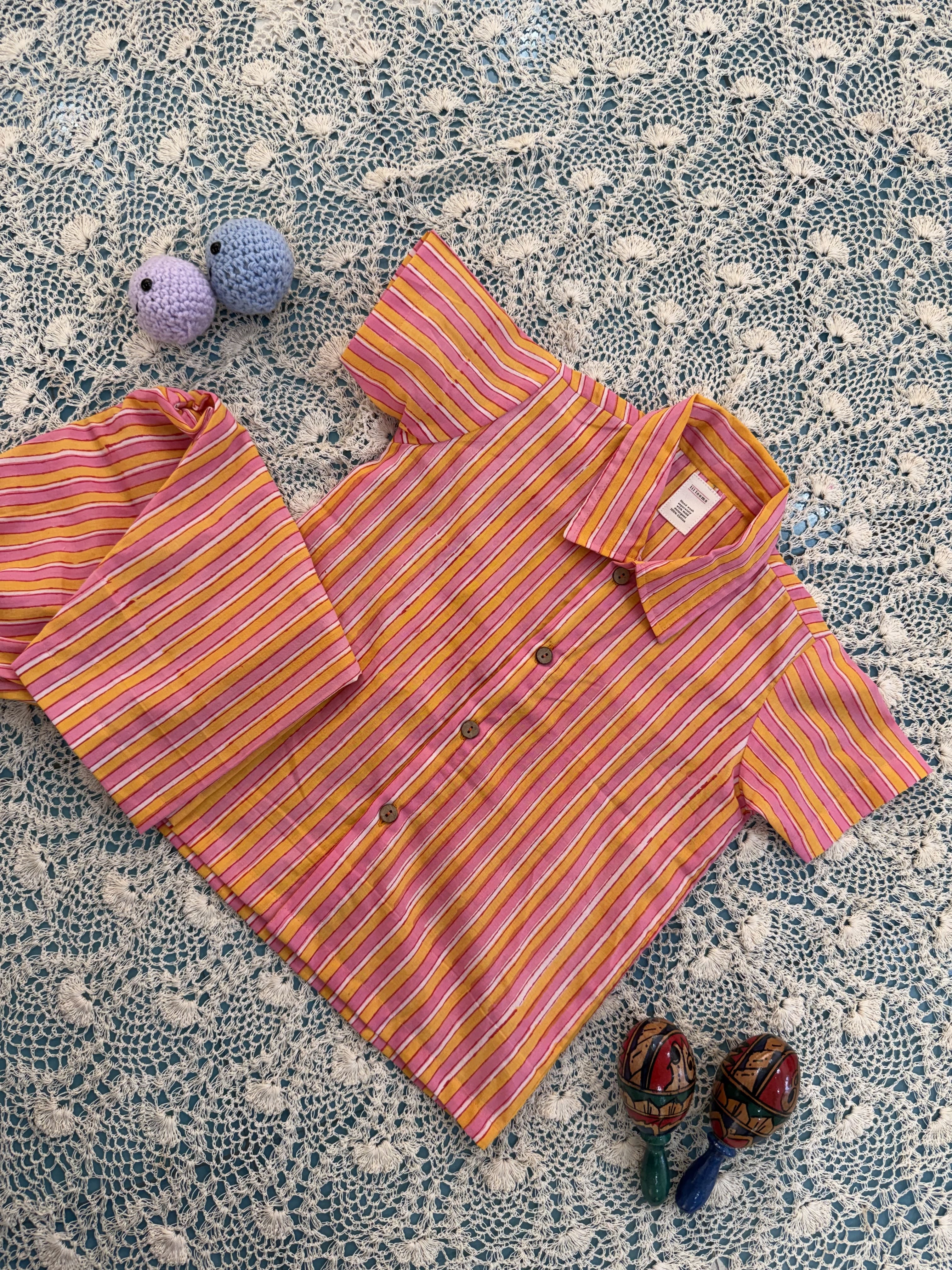 Pink and yellow striped pajama set on a textured surface with toys.