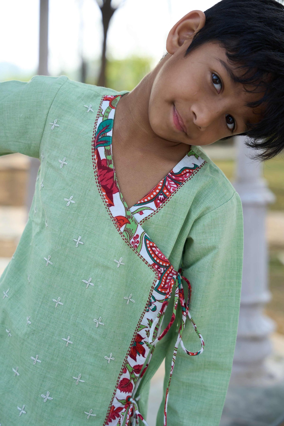 Child wearing a green traditional outfit with a colorful neckline in an outdoor setting